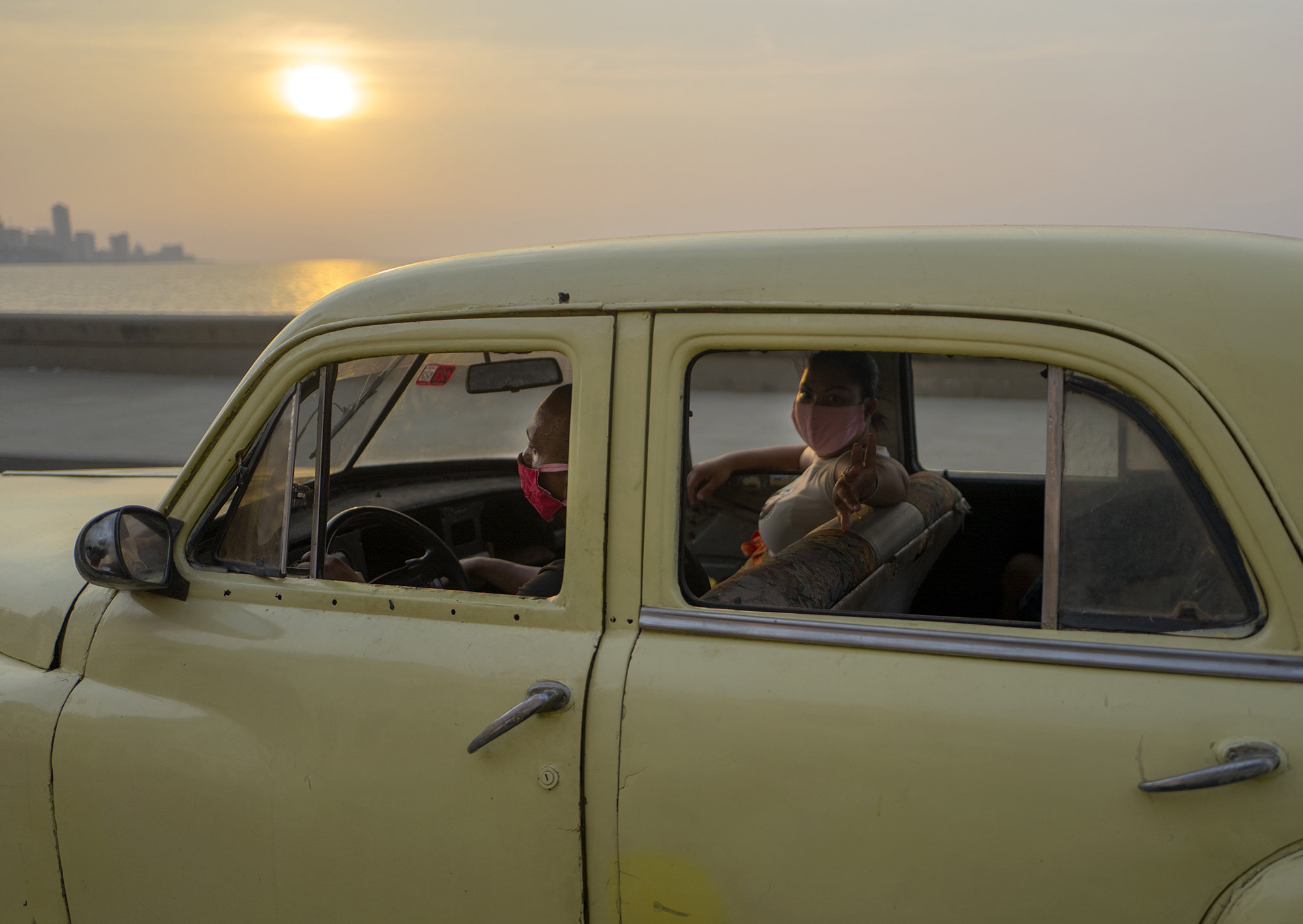  Cubanos con el tapabocas puesto dentro de un carro americano clsico recorren a lo largo del Malecn durante el atardecer en La Habana, Cuba, Abril 14, 2020. 