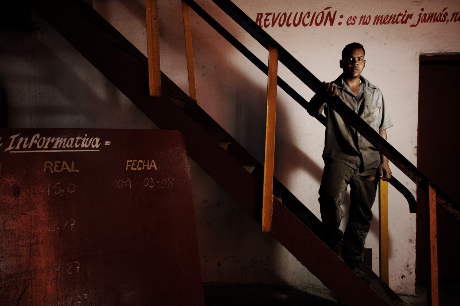  Lazaro,18, assistant electrician, stands on a stairway that bears a slogan by Fidel Castro: Revolution is never to lie!, in a sugarcane factory, where he started working one year ago. 