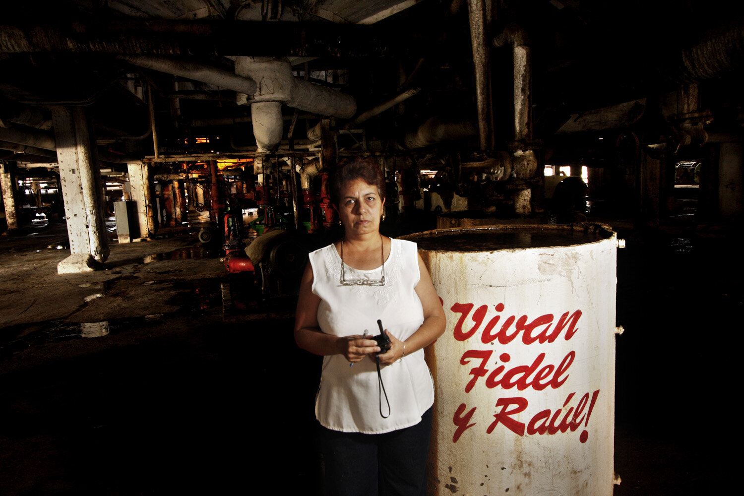  Mayra, 52, director of ta sugarcane factory, poses for a portrait next to a tank that has written on it: Long Live Fidel and Raul (Vivan Fidel y Raul). She has been working for 28  years in the sugarcane industry. 