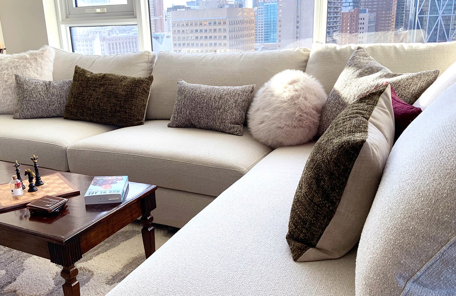 Light neutral furnishings, warm wood tones, and soft colourful accents create a comfortable seating area designed to showcase the city skyline views.