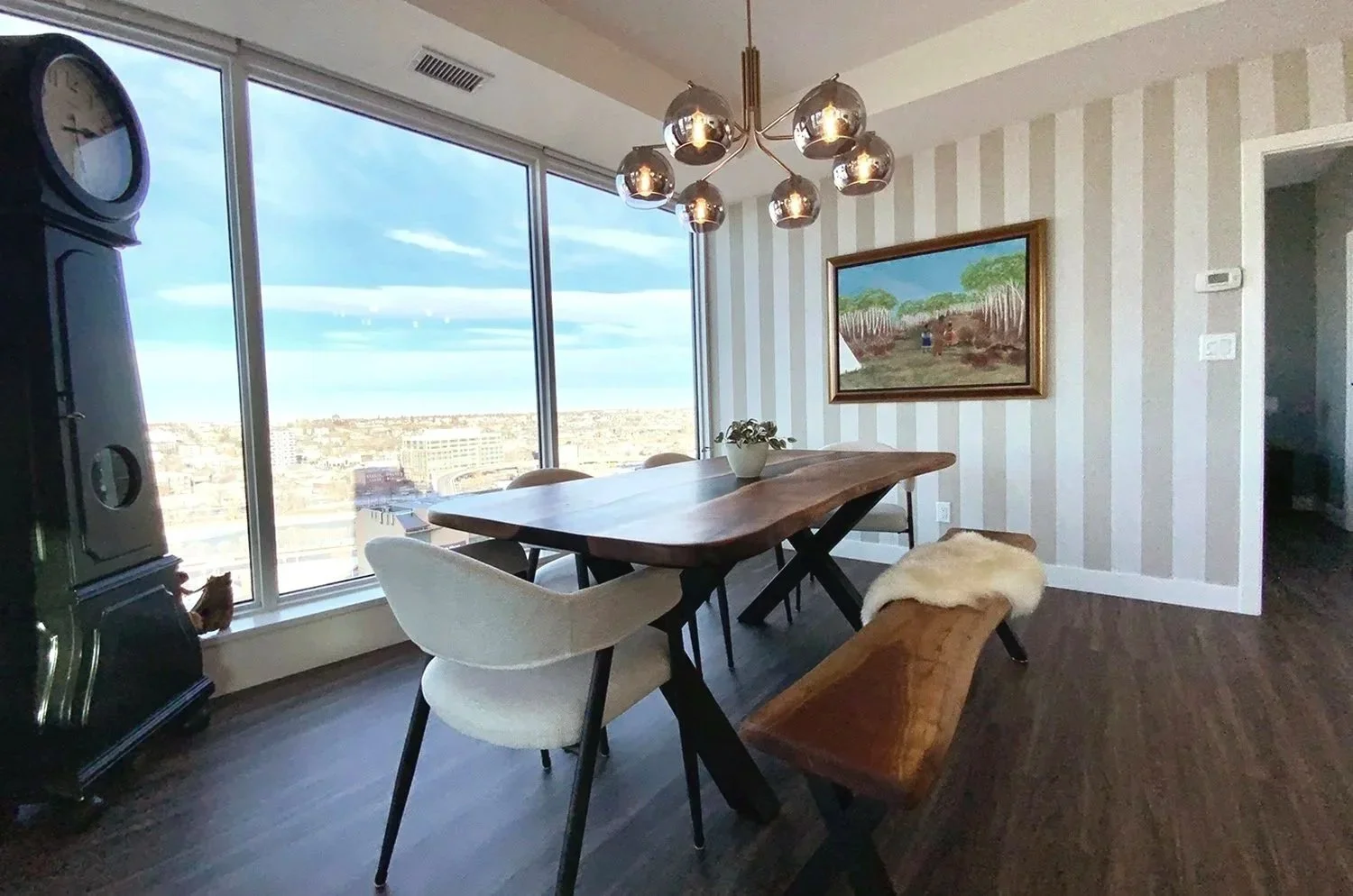 This eclectic dining room design mixes antique furnishings with modern elements, complemented by striped wallpaper to create a warm, stylish entertaining space with city views