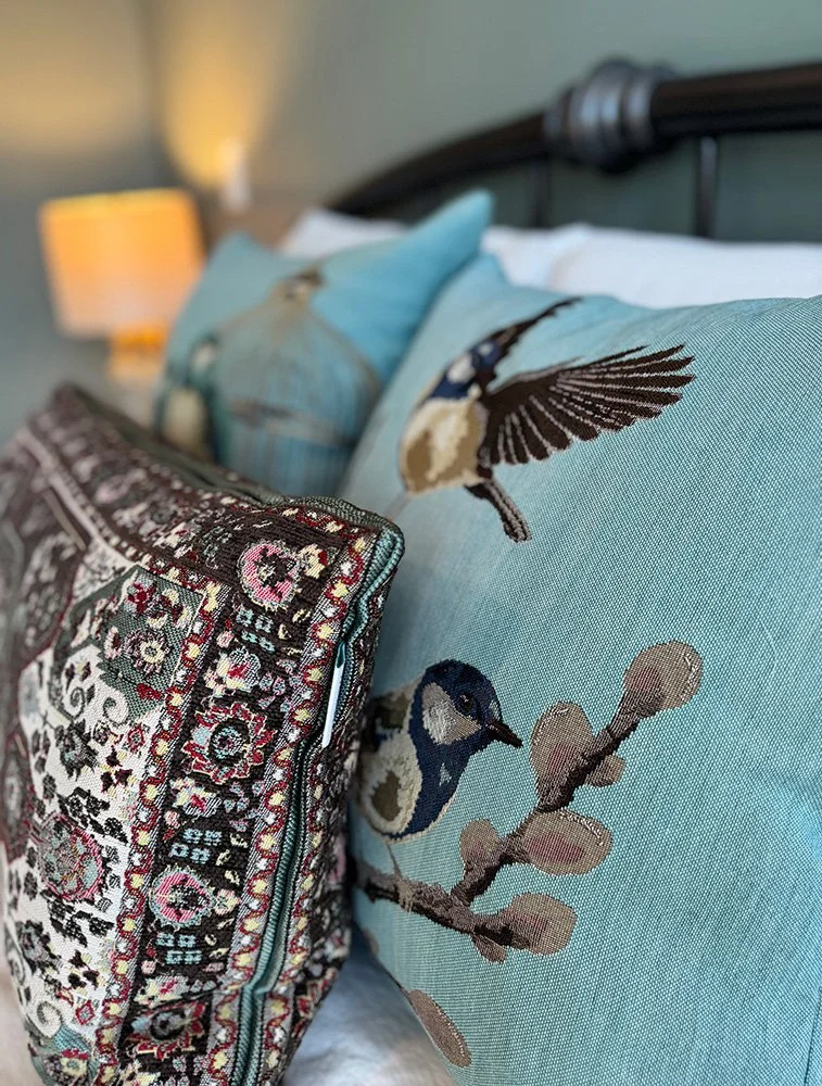 This green bedroom design features brocade accent pillows with nature-inspired patterns, creating a layered, eclectic space rich in character, texture, and warmth