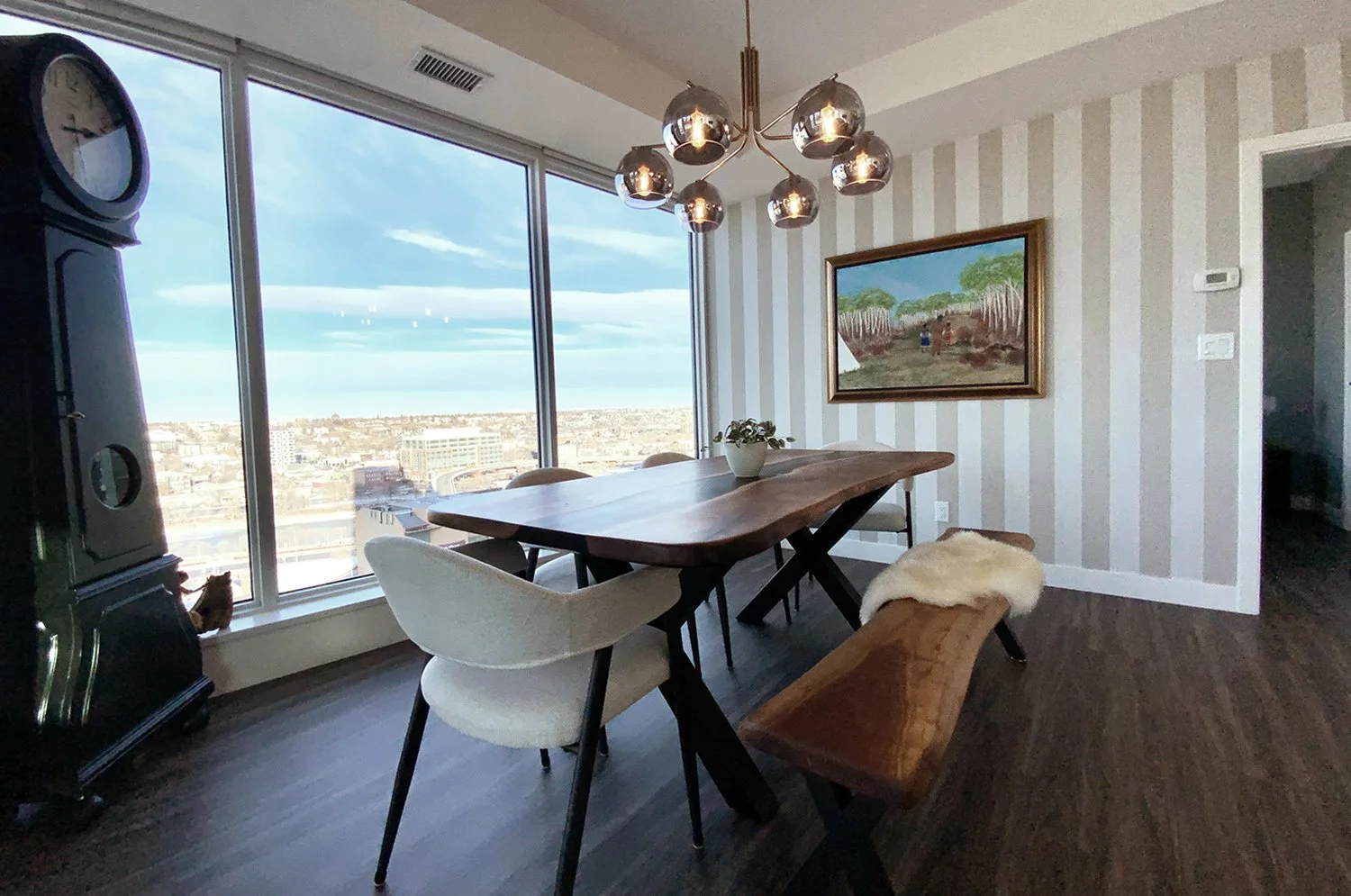 This eclectic dining room design mixes antique furnishings with modern elements, complemented by striped wallpaper to create a warm, stylish entertaining space with city views