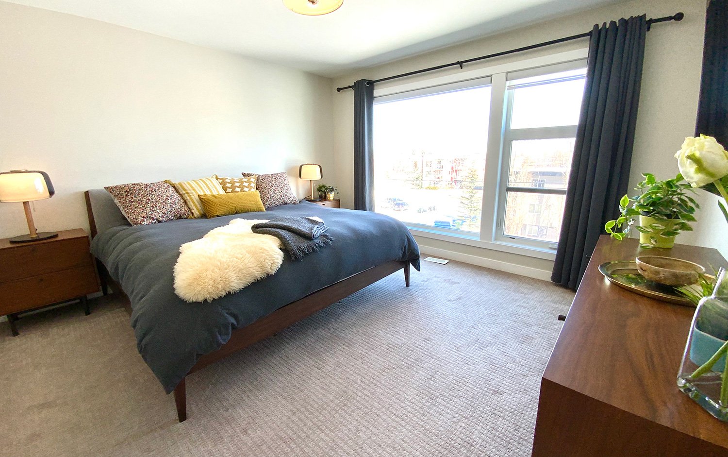Simple and contemporary bedroom with neutrals and midcentury furnishings are accented with vibrant pillows and textured blankets to create warmth.