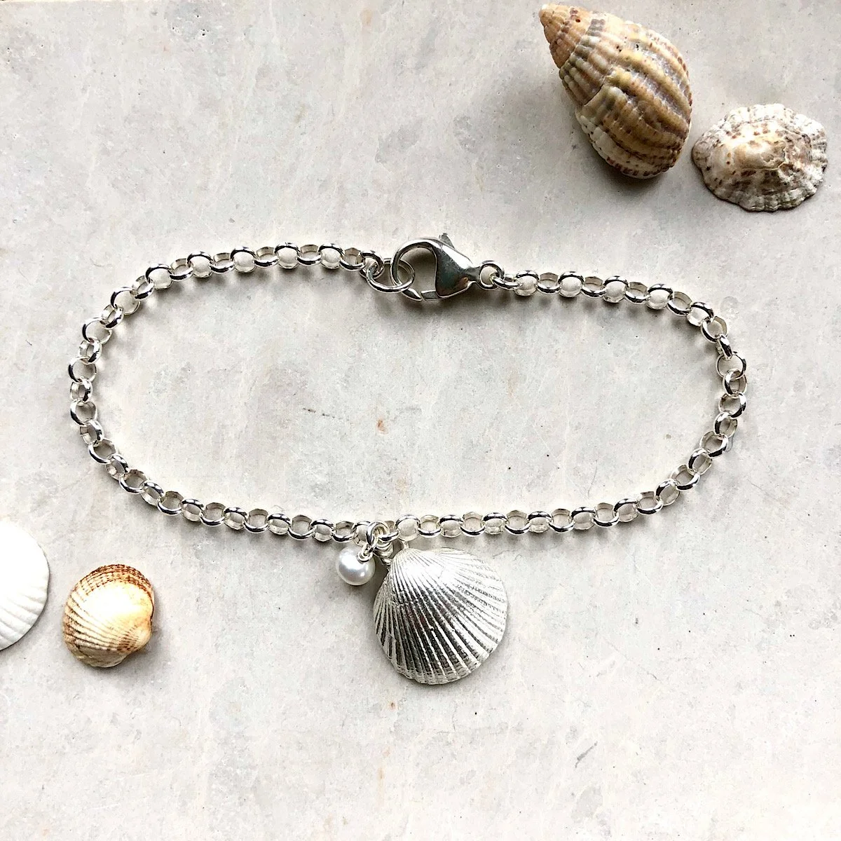 sterling silver shell bracelet - with cockle shell and ivory pearl - on a wooden board with sea shells - sea inspired jewellery