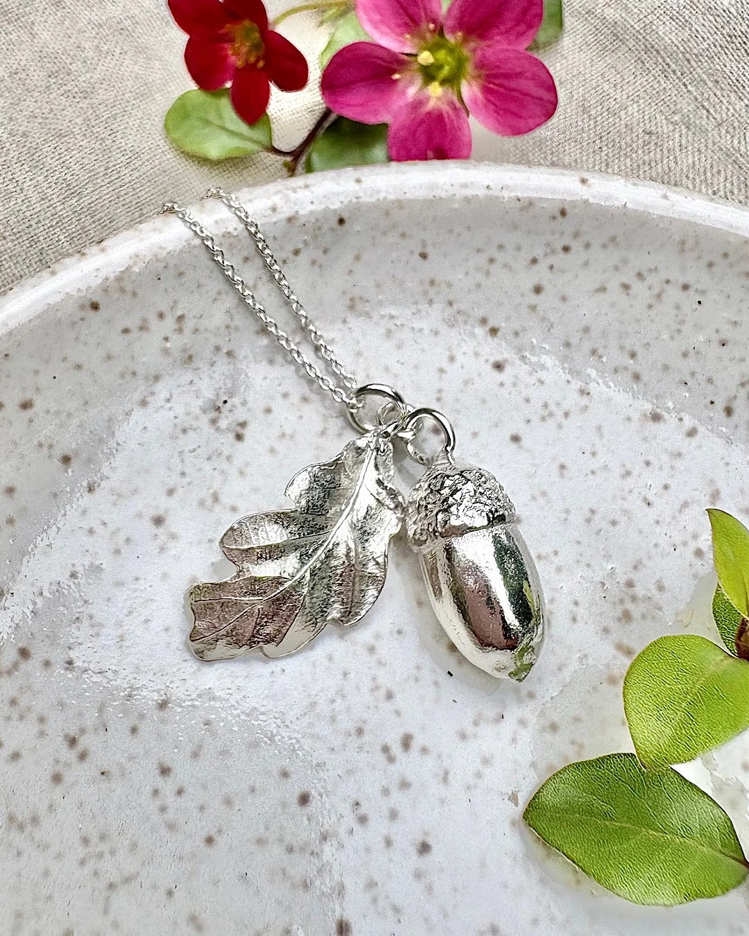sterling silver acorn necklace - handmade jewellery botanical inspired - on ceramic tray with flowers.