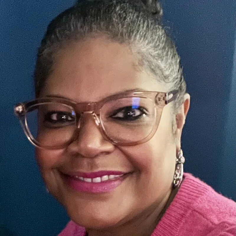 Professional Headshot of an African American Woman looking forward. She is wearing glasses and has her her up in a bun.