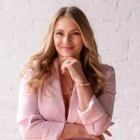 Megan wearing a pink suite, looking at the camera, with her hand under her chin