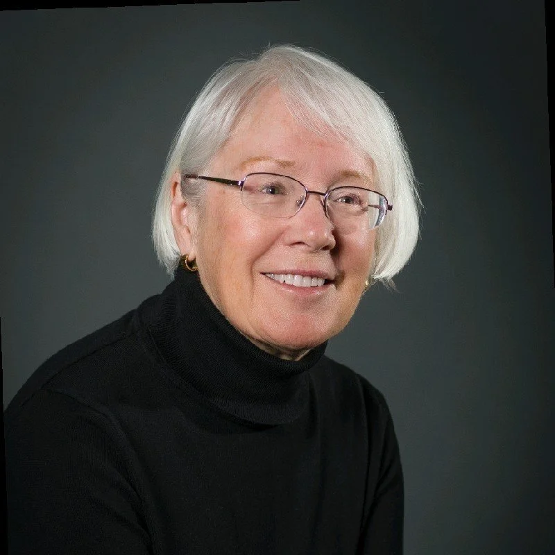 Professional portrait of a woman with short hair, wearing glasses, in a black turtle neck sweater