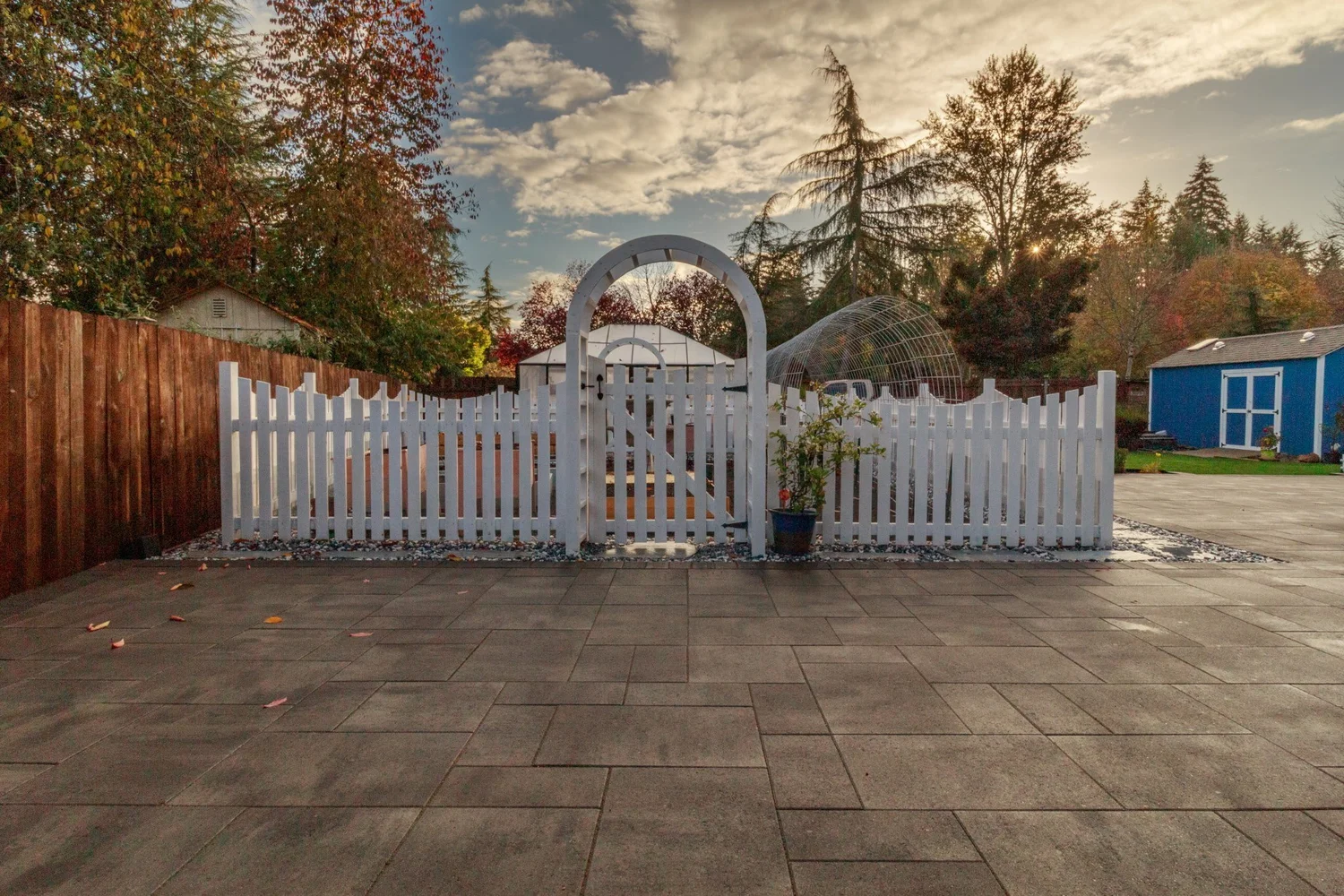 Paver patio leading to a white arbor gate and picket fence in Lacey, WA