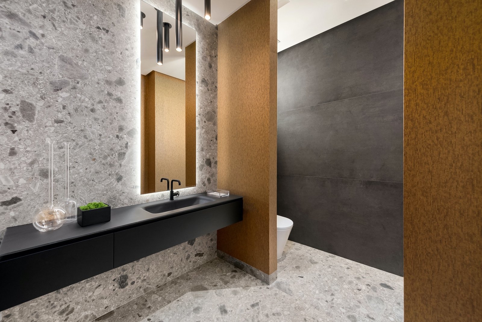Modern bathroom interior with stone wall, LED-lit mirror, black countertop with a sink, and decorative items.