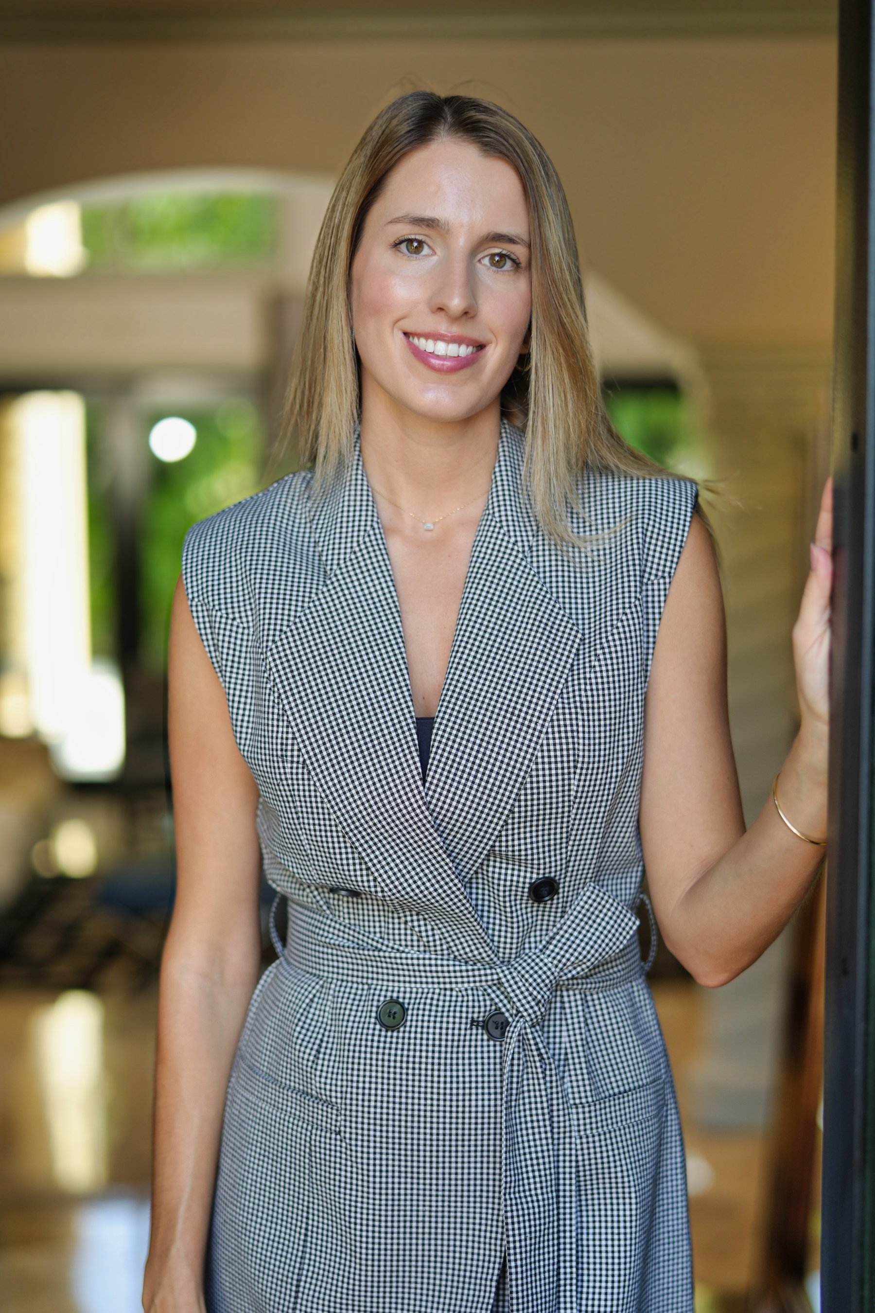 Smiling woman in checkered dress standing indoors.