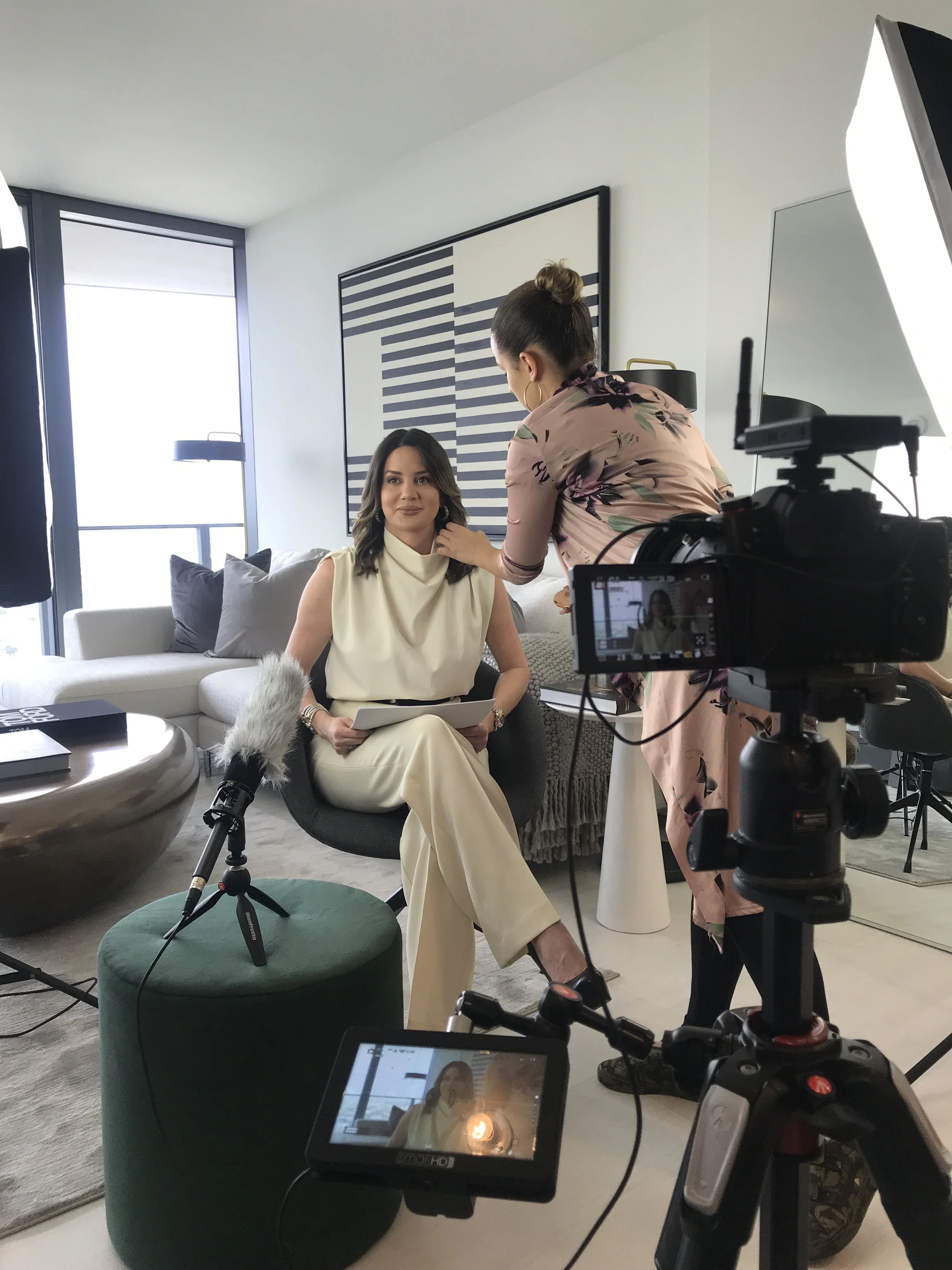 Woman getting makeup touch-up in a home studio setup, with cameras and lighting equipment around.
