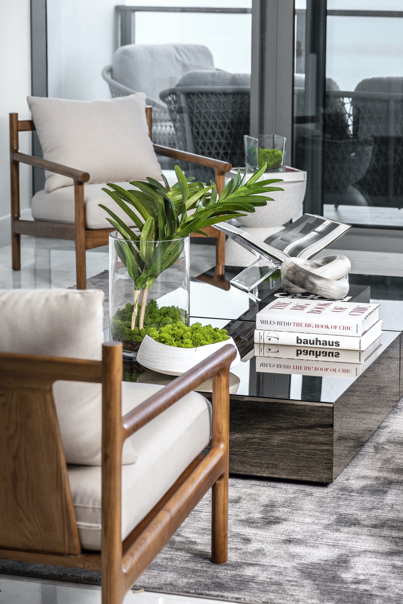 Modern living room with wooden armchairs, glass coffee table, decorative books and a leafy plant centerpiece. 1 OAK Studios, photo, video, drone, real estate photography and video.