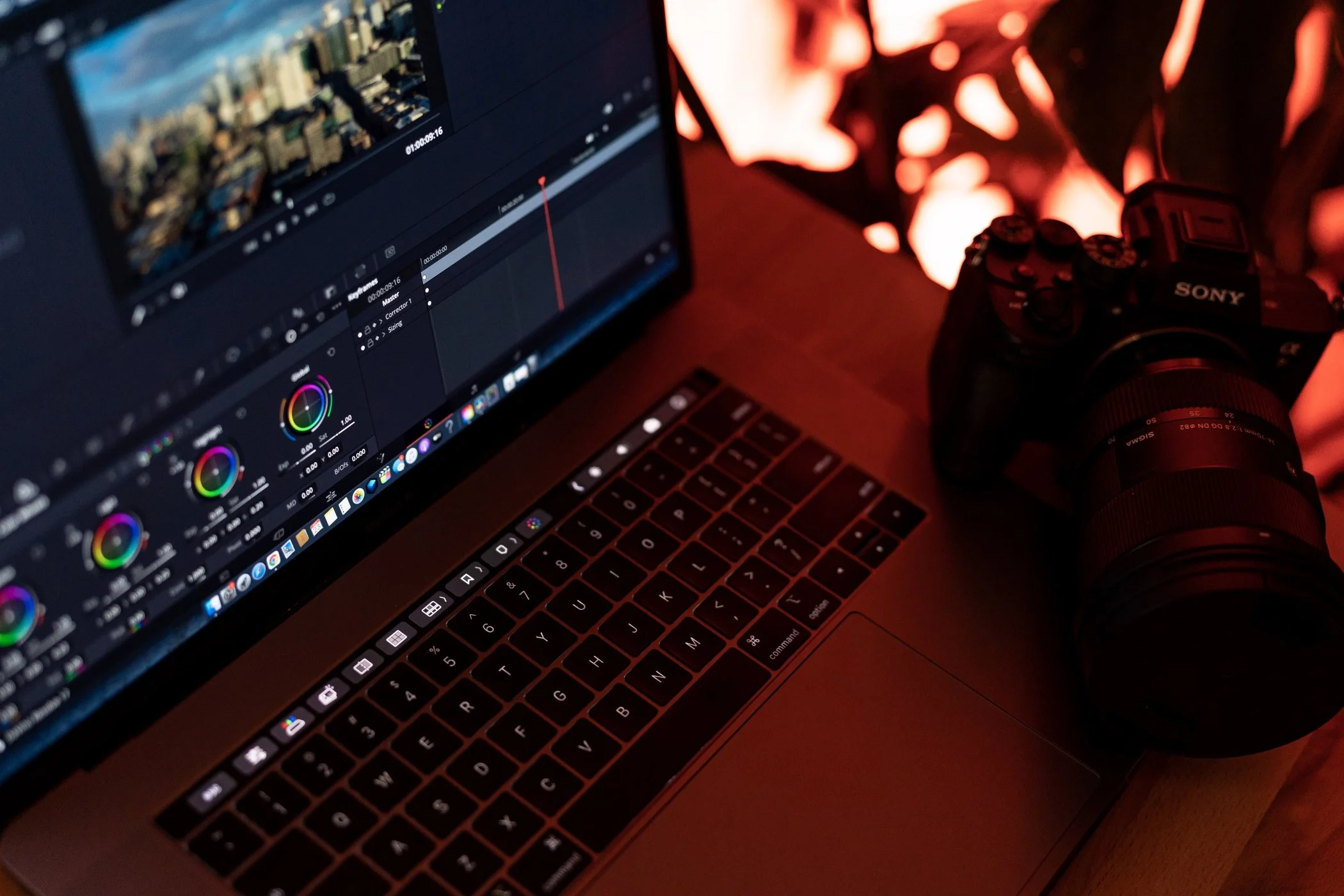 A laptop with a video editing program open on the screen, a Sony camera placed next to the laptop, and a fire feature in the background emitting orange flames.