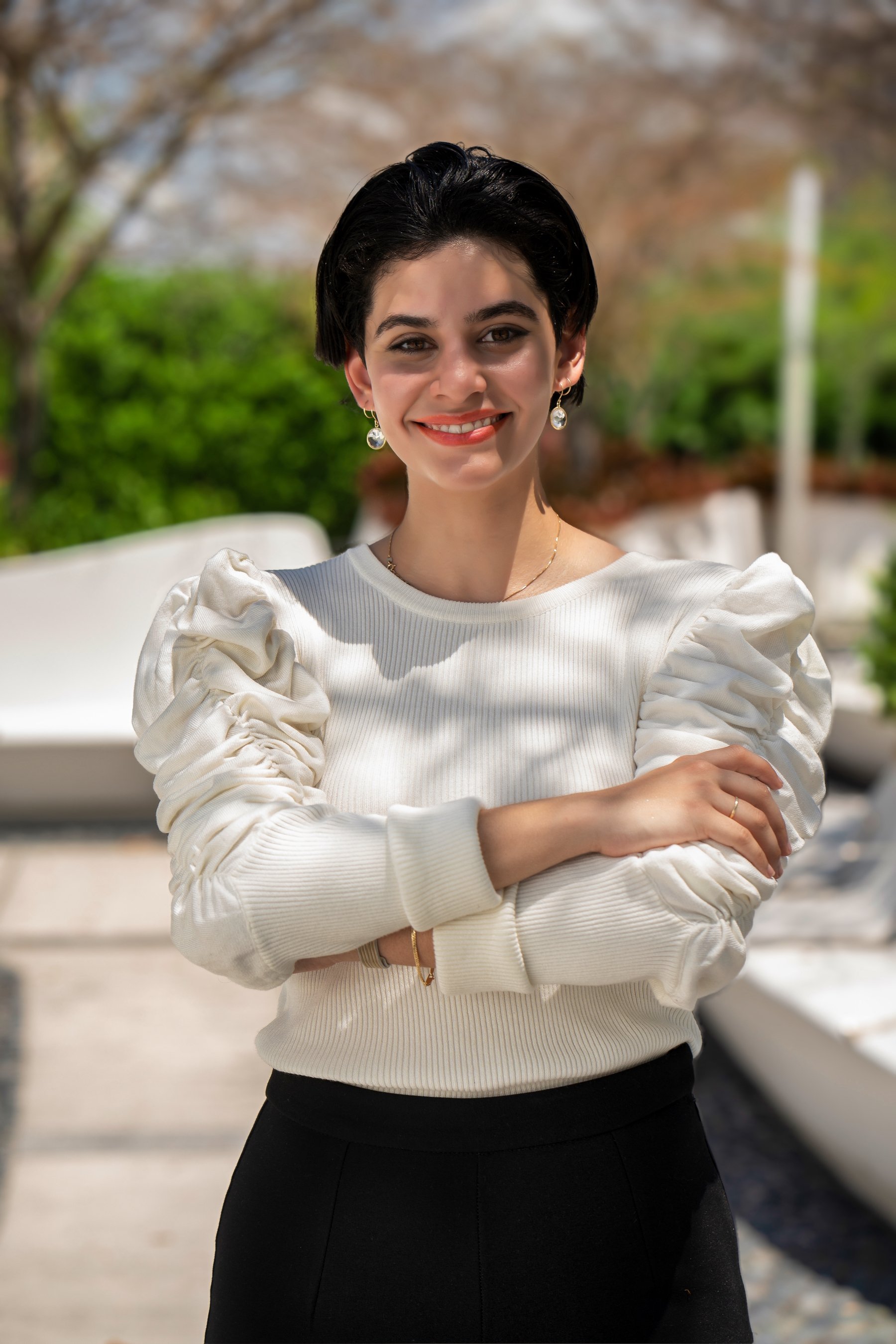Woman with short hair wearing a white blouse with puffed sleeves, smiling outdoors. 1 OAK Studios, photo, video, drone, real estate photography and video.