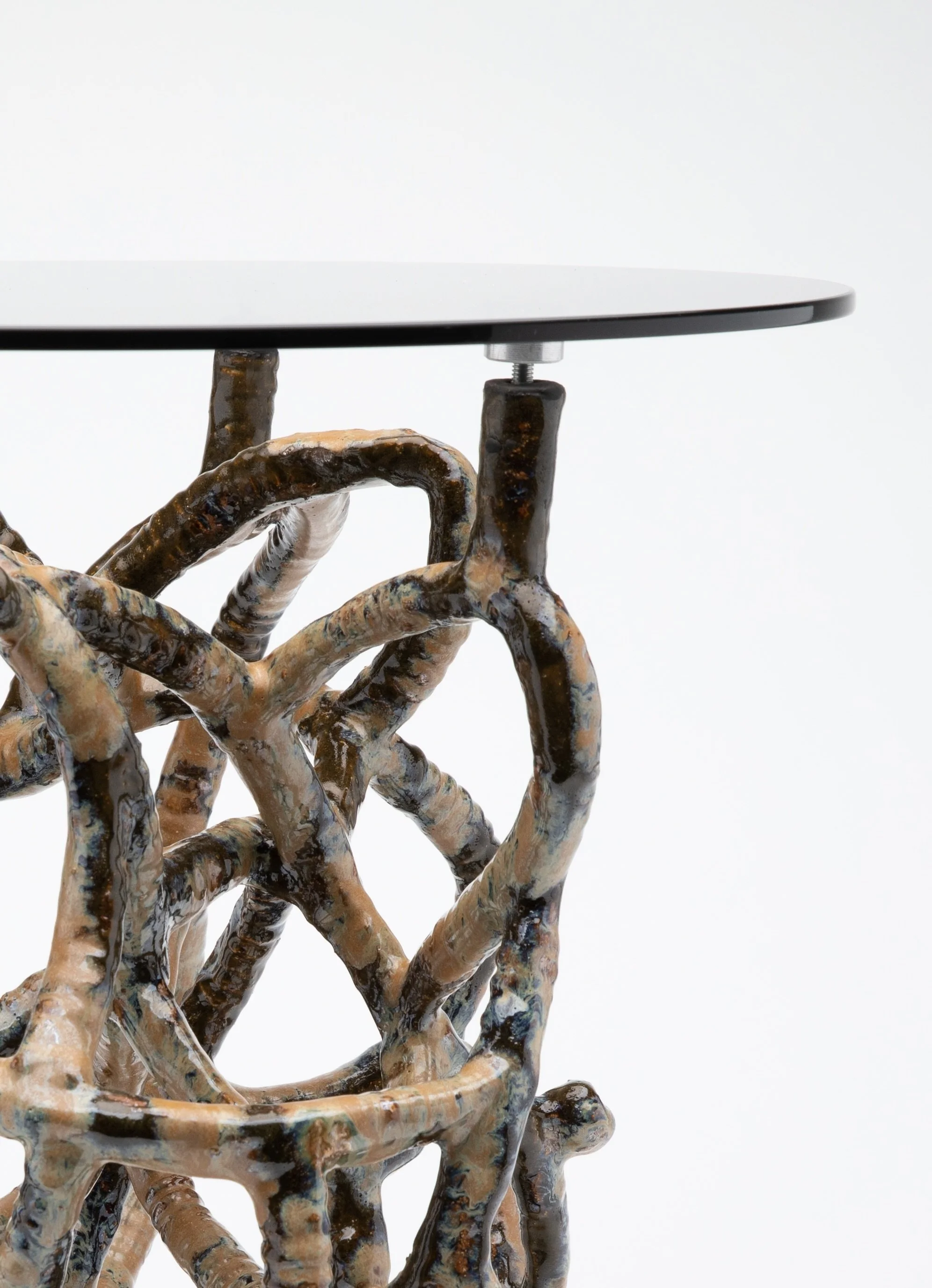 Close-up of a sculpted ceramic table base integrated with a modern, round table top, supported by intricately textured, multi-colored legs.