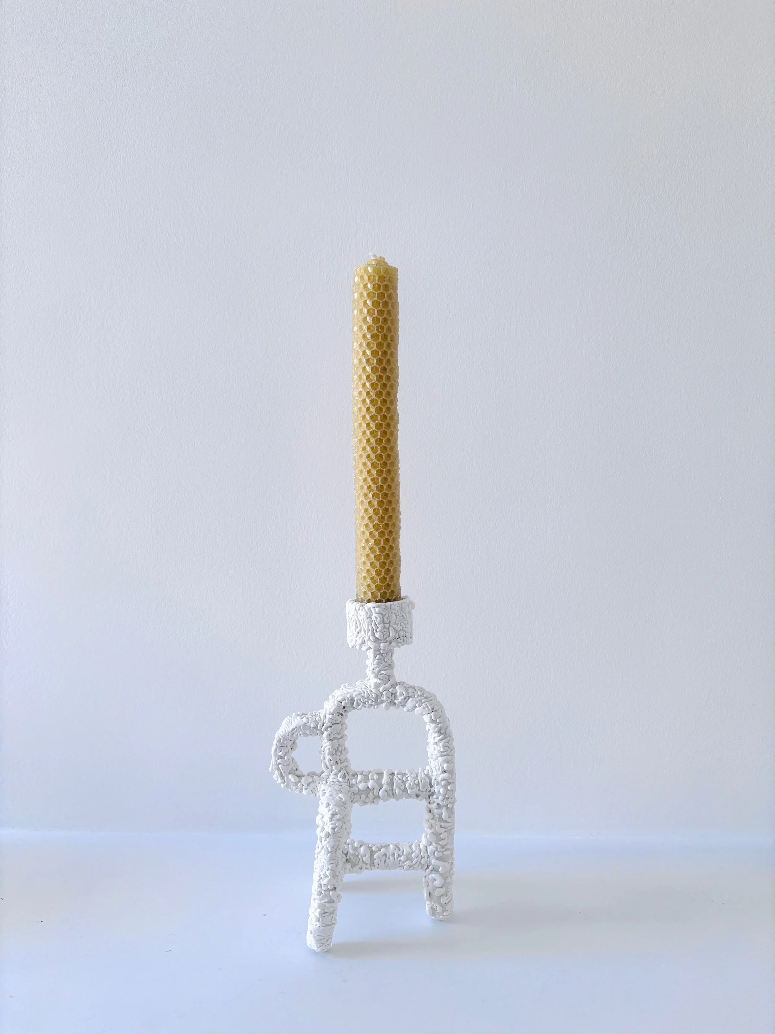 A decorative white glazed ceramic candle holder with honeycomb beeswax candle against a white background