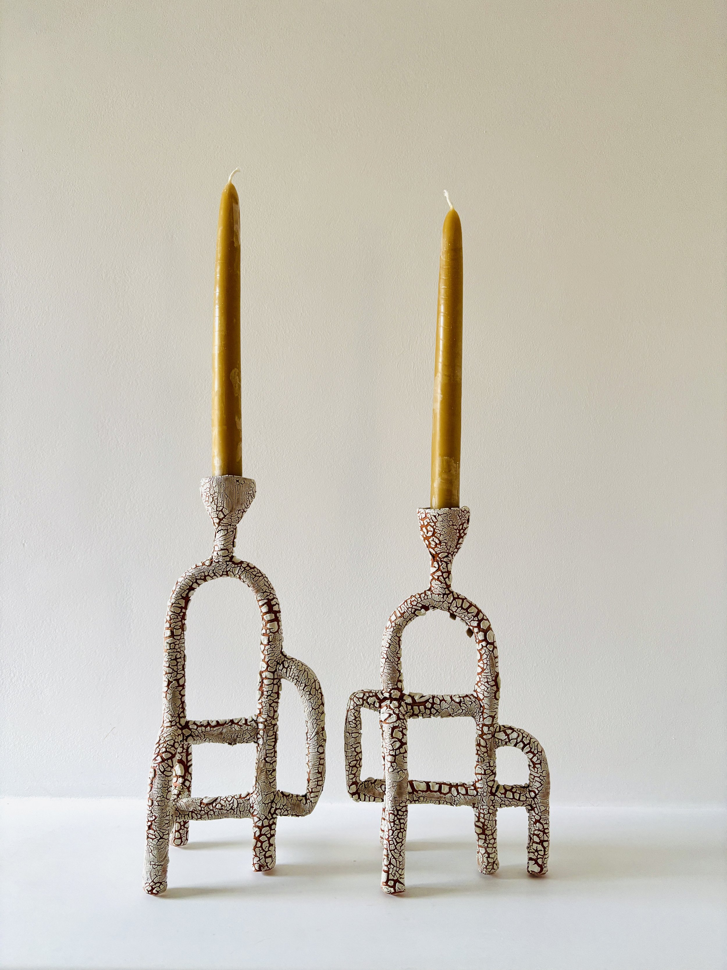 A set of two ceramic candle holders in various sizes with textured, cracked, beige and white patterns, standing on a white surface against a neutral background.