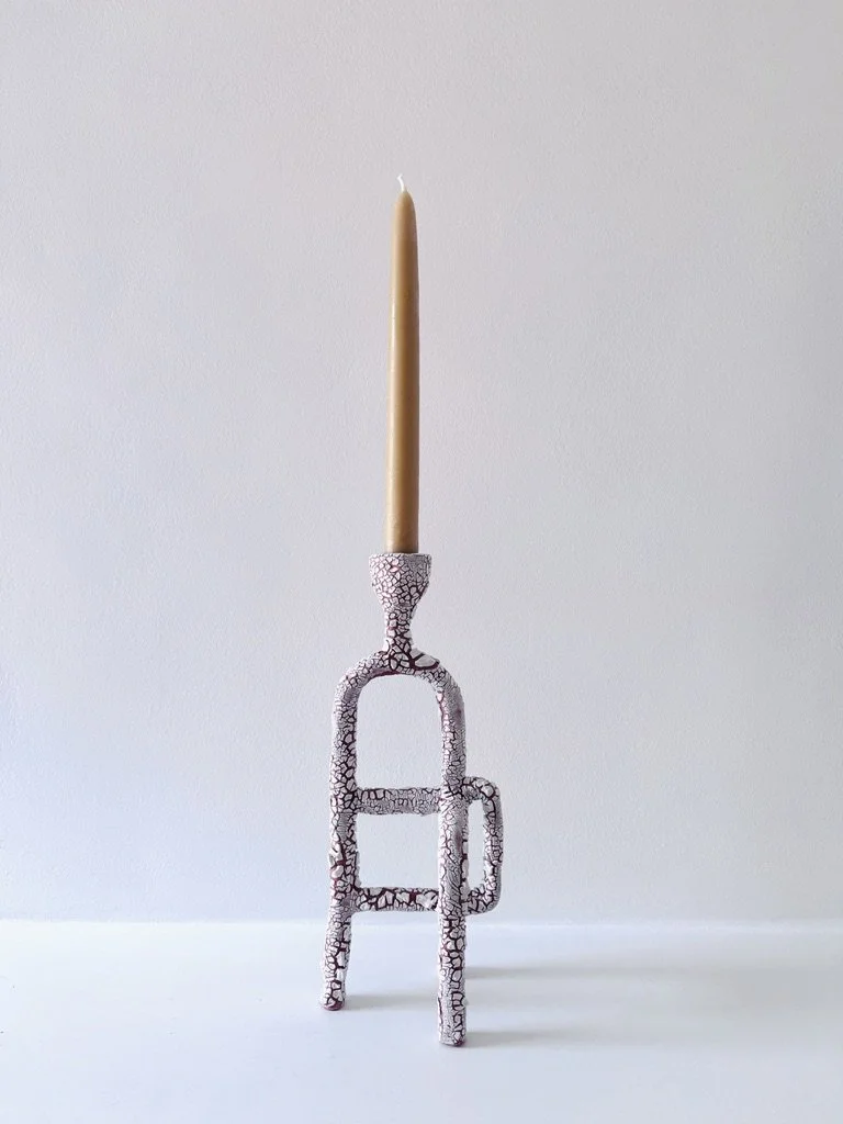 A decorative candle holder with a crackled glaze with a tall, yellow beeswax candle on top, placed against a plain white background.