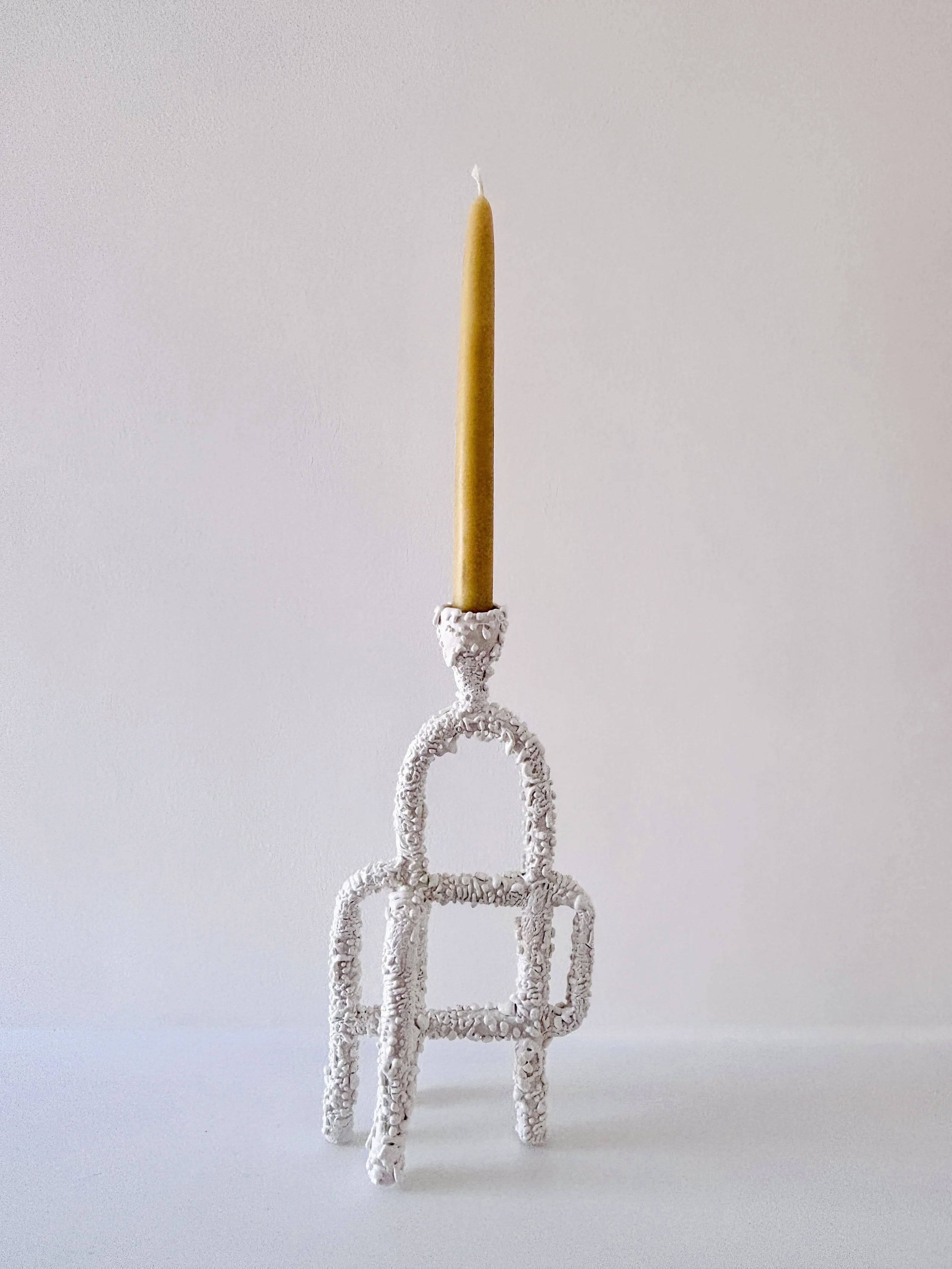 A decorative white glazed ceramic candle holder with yellow beeswax candle against a white background