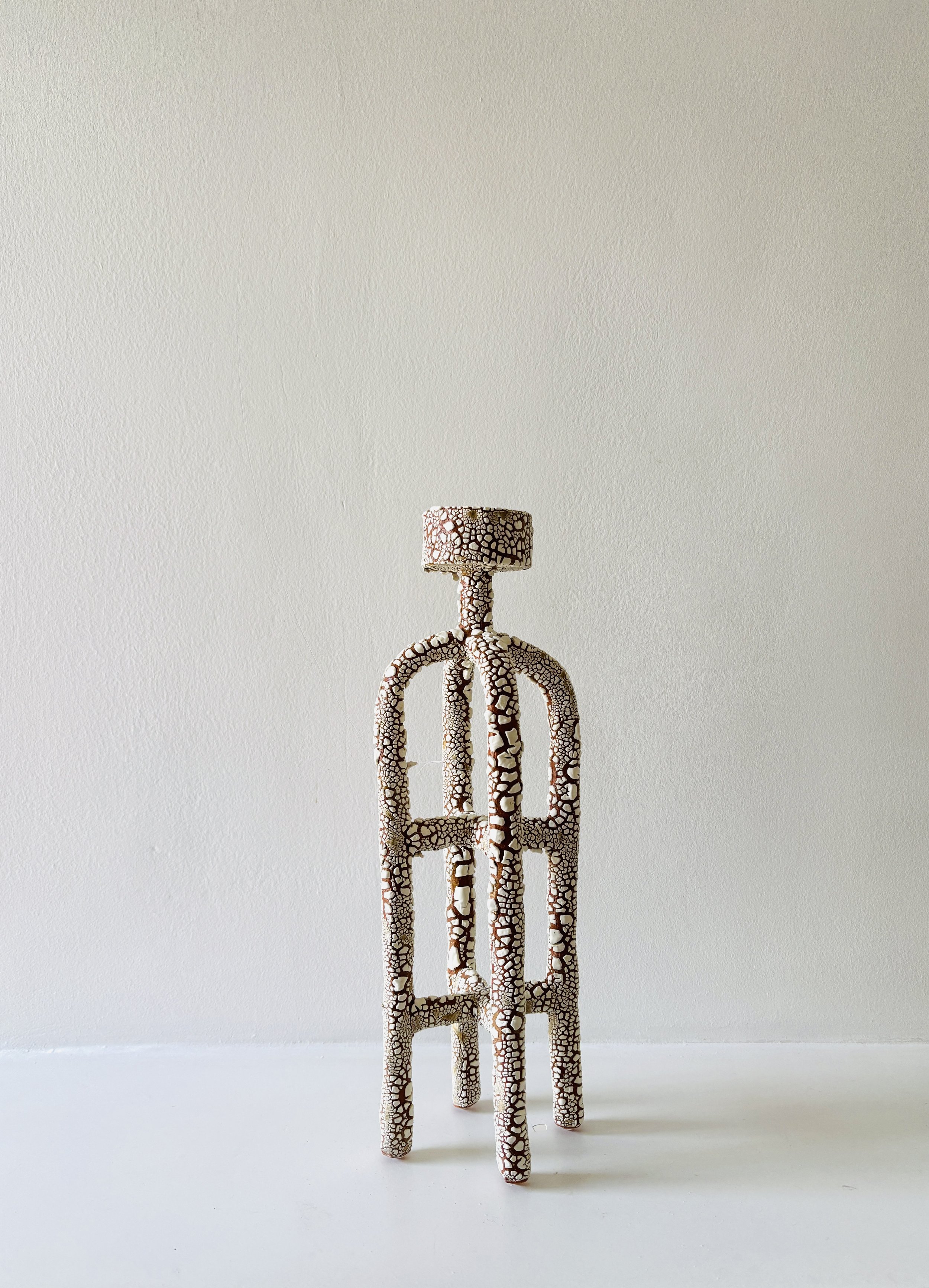 Abstract sculptured tea light holder with a textured, cracked surface pattern, standing on a white floor against a plain white wall.