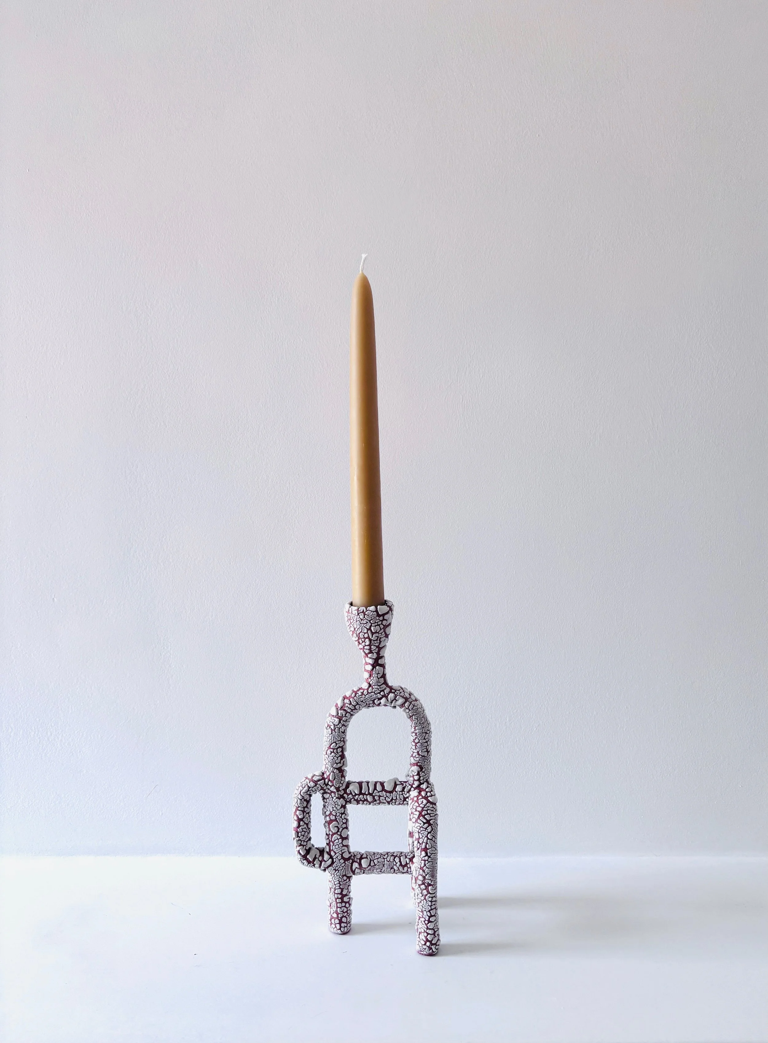 A decorative candle holder with a crackled glaze with a tall, yellow beeswax candle on top, placed against a plain white background.
