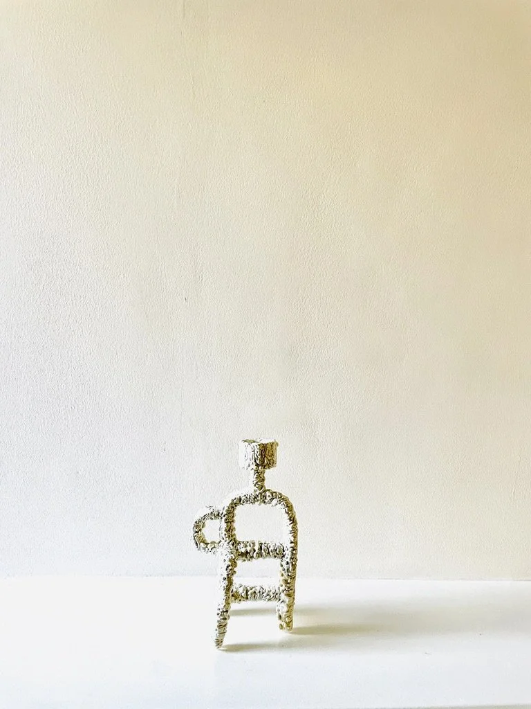 Small ceramic sculpture candlestick with a white textured glaze  against a plain beige wall.