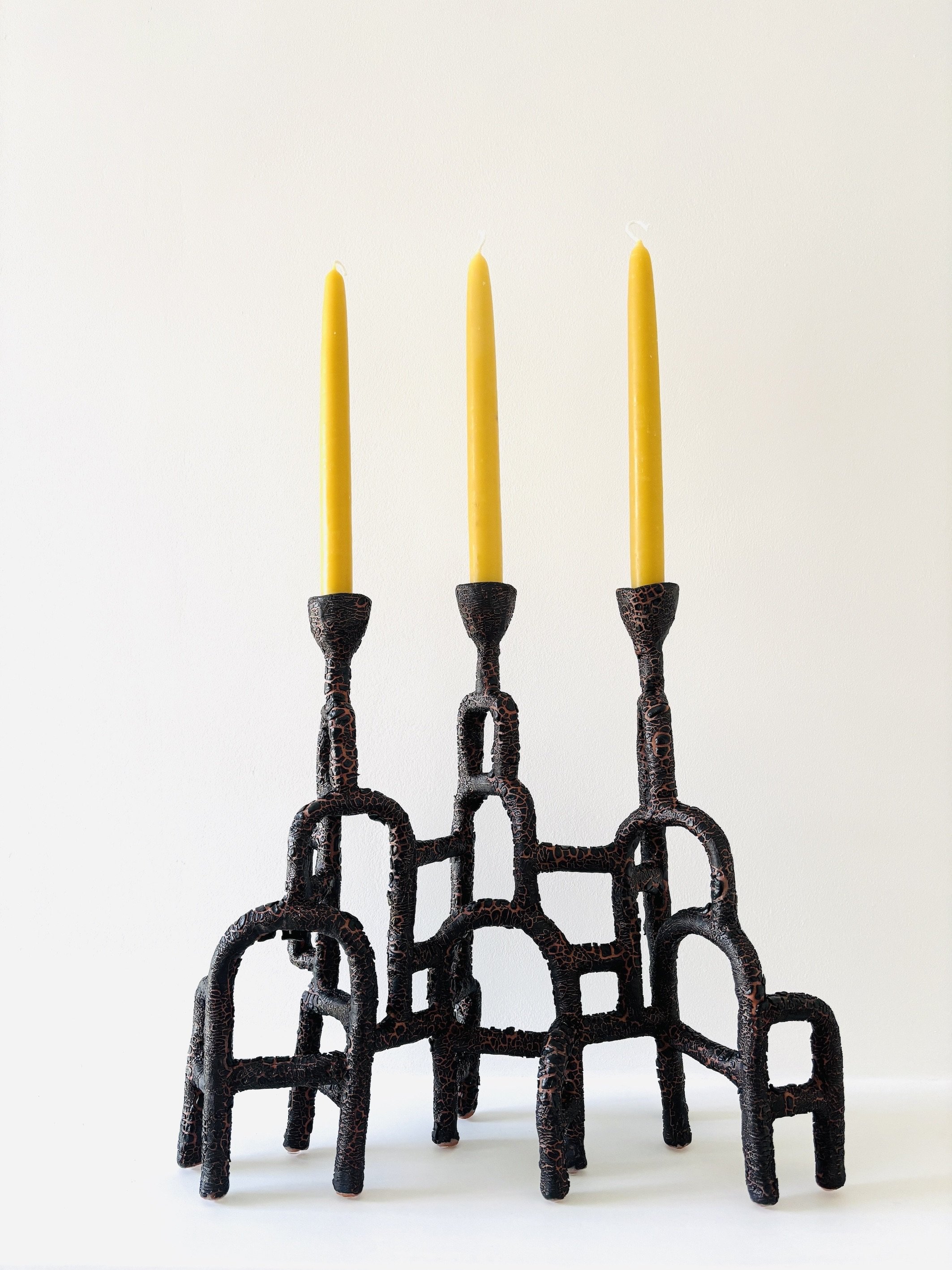 A collection of black, textured, abstract sculptures arranged in a pyramid shape with three yellow candles on top.
