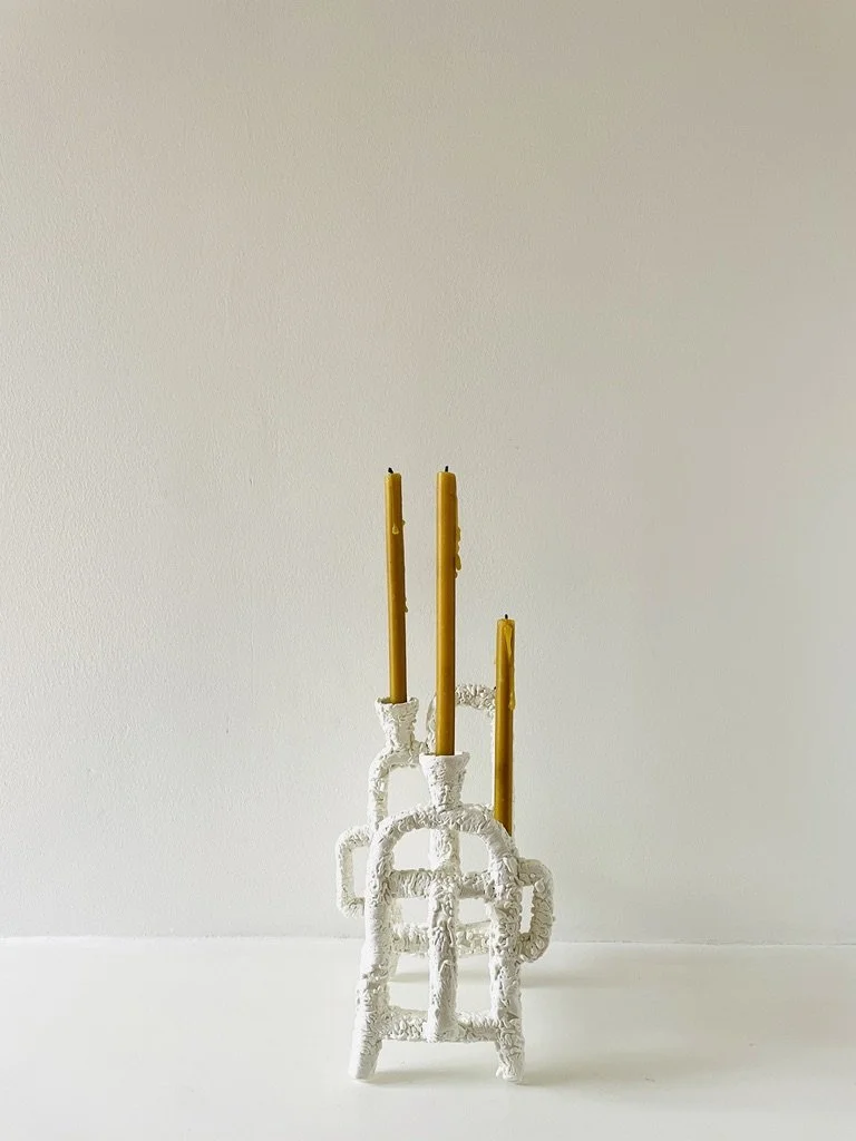 White decorative candle holder with three yellow candles, set against a plain wall.