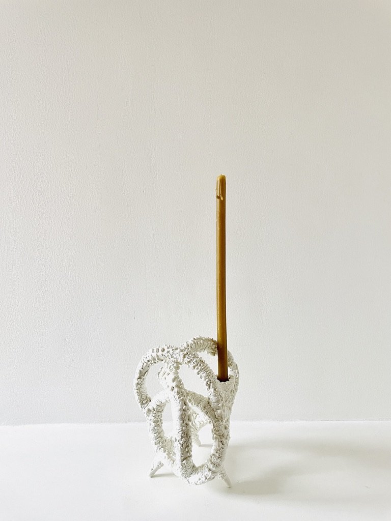 A white decorative holder with a curly, textured design holding a single yellow candle against a plain white background.