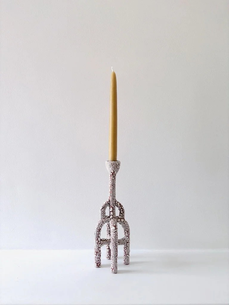a tall yellow beeswax  candle placed upright on a ceramic candlestick holder with multiple arches and intricate patterns