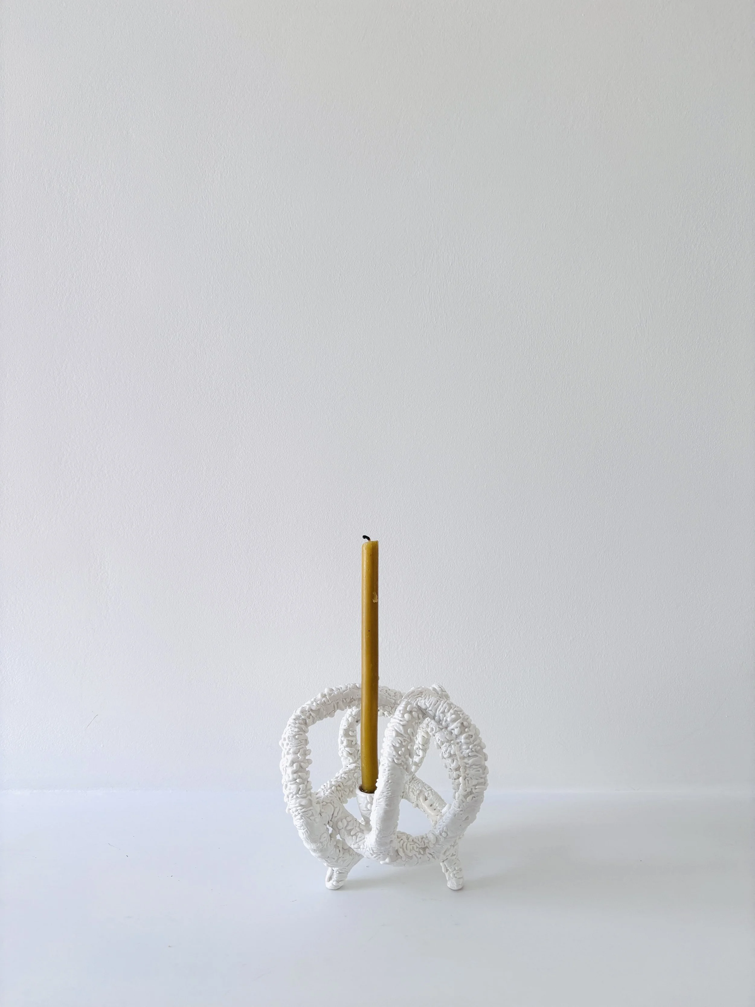 A tangled ceramic sculpture, a yellow candle upright through the middle, and a tall, thin yellow candle extending upward from the center.