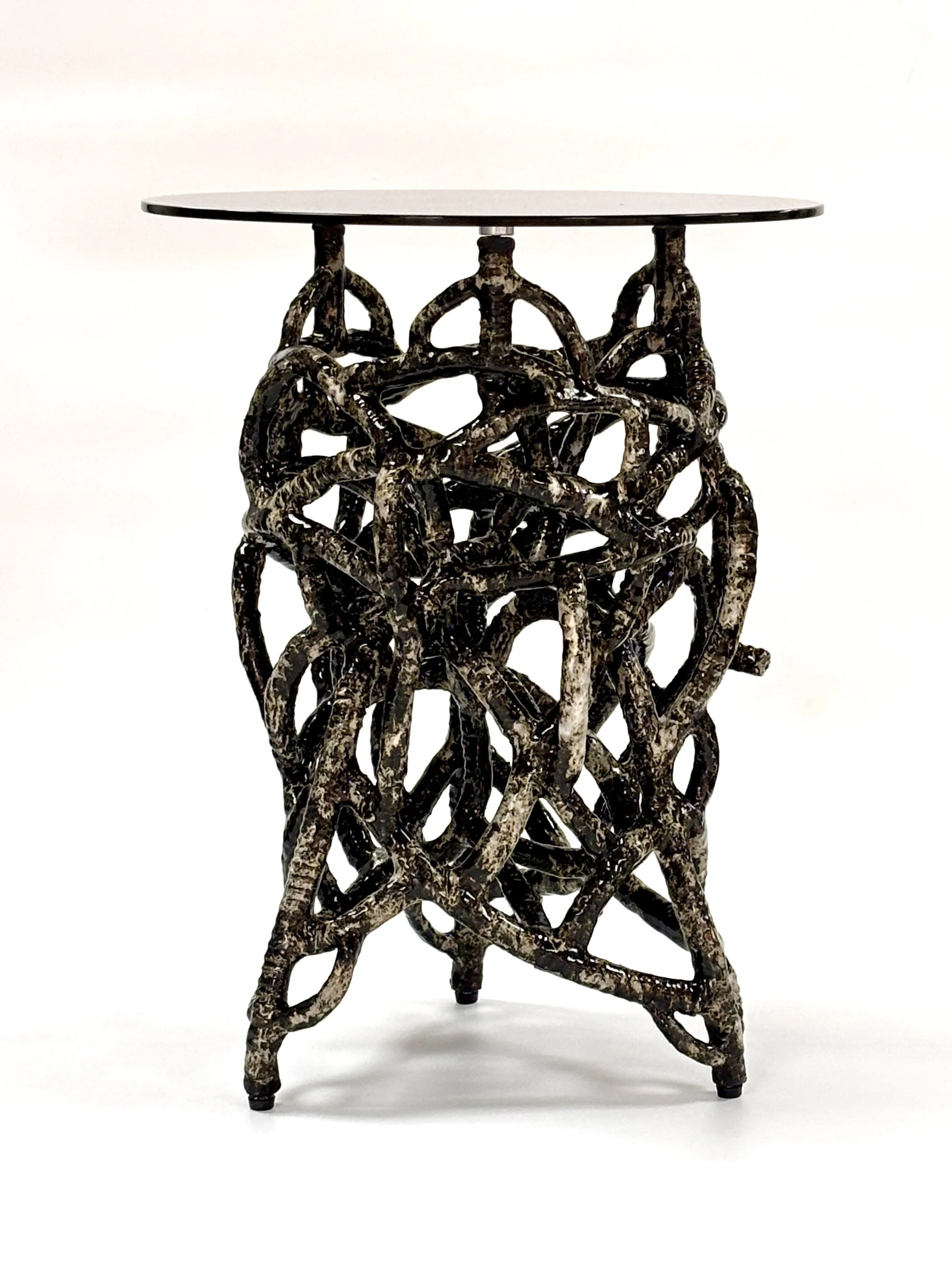 A small table with a base made of intertwined, branch-like sceramic tubes  and a flat round glass top.