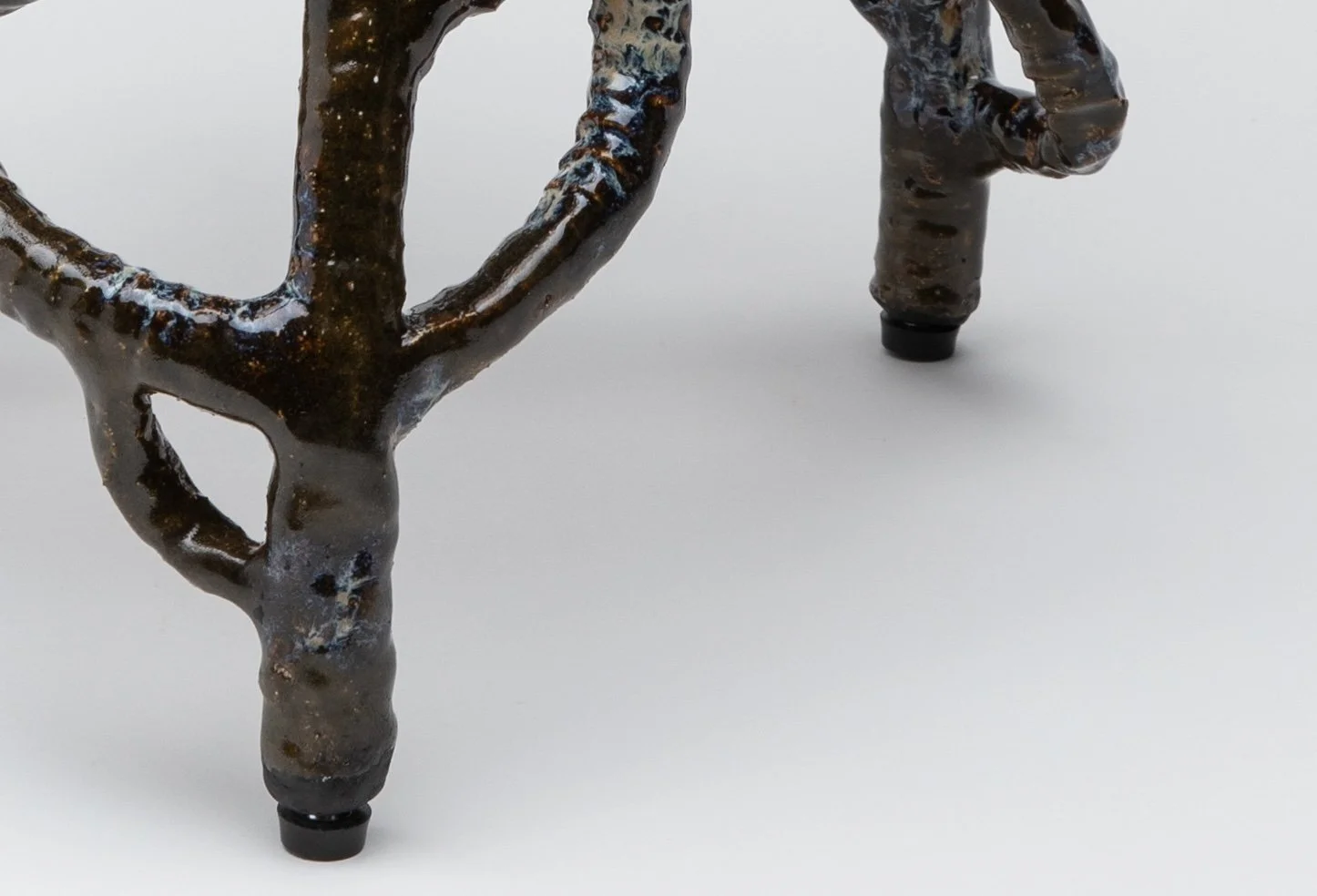 Close-up of a decorative metal sculpture resembling a stylized animal, with two legs and a curved body, set against a plain white background.
