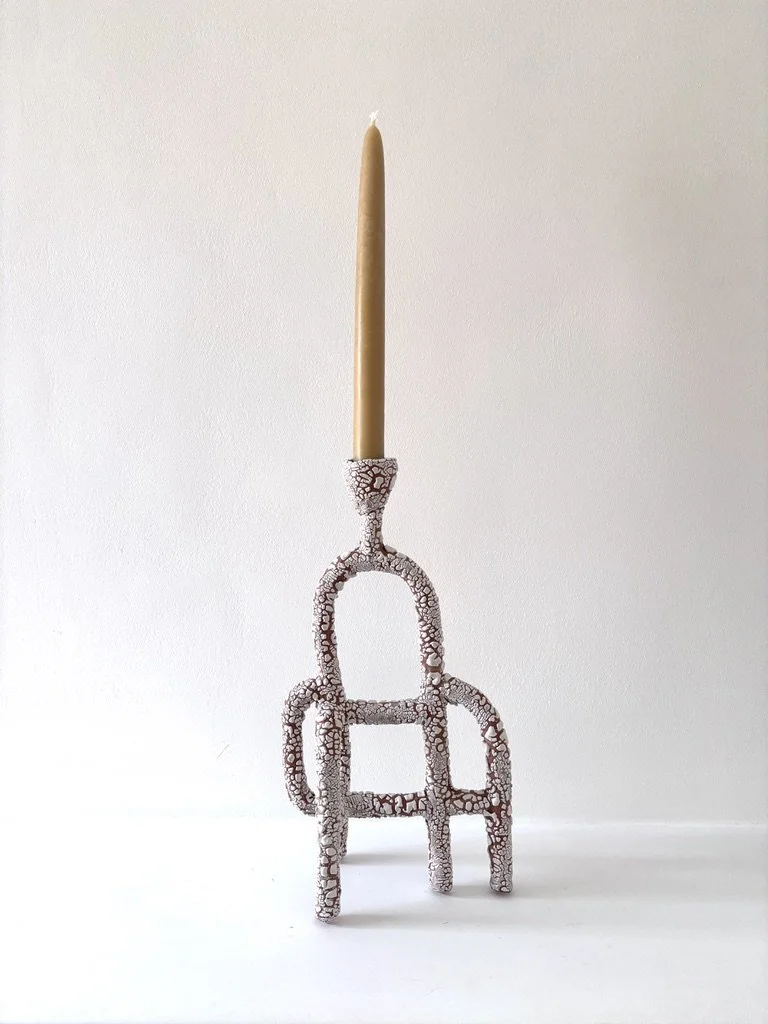 A decorative candle holder with a single beige taper candle on top, featuring a textured surface resembling broken or cracked material, placed against a plain white background.