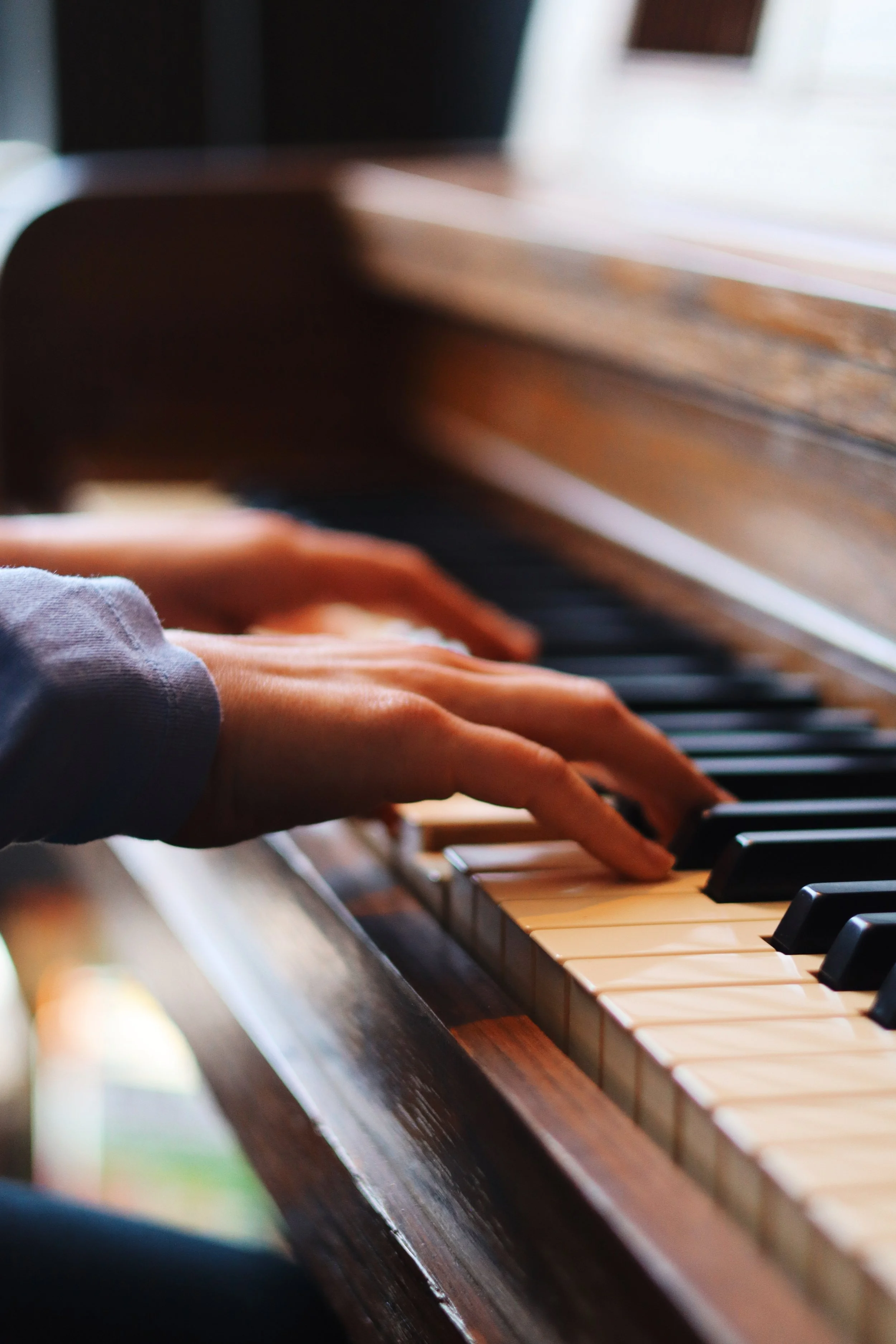 Close-up of a person's hand playing the piano on wooden keys with black and white keys visible.