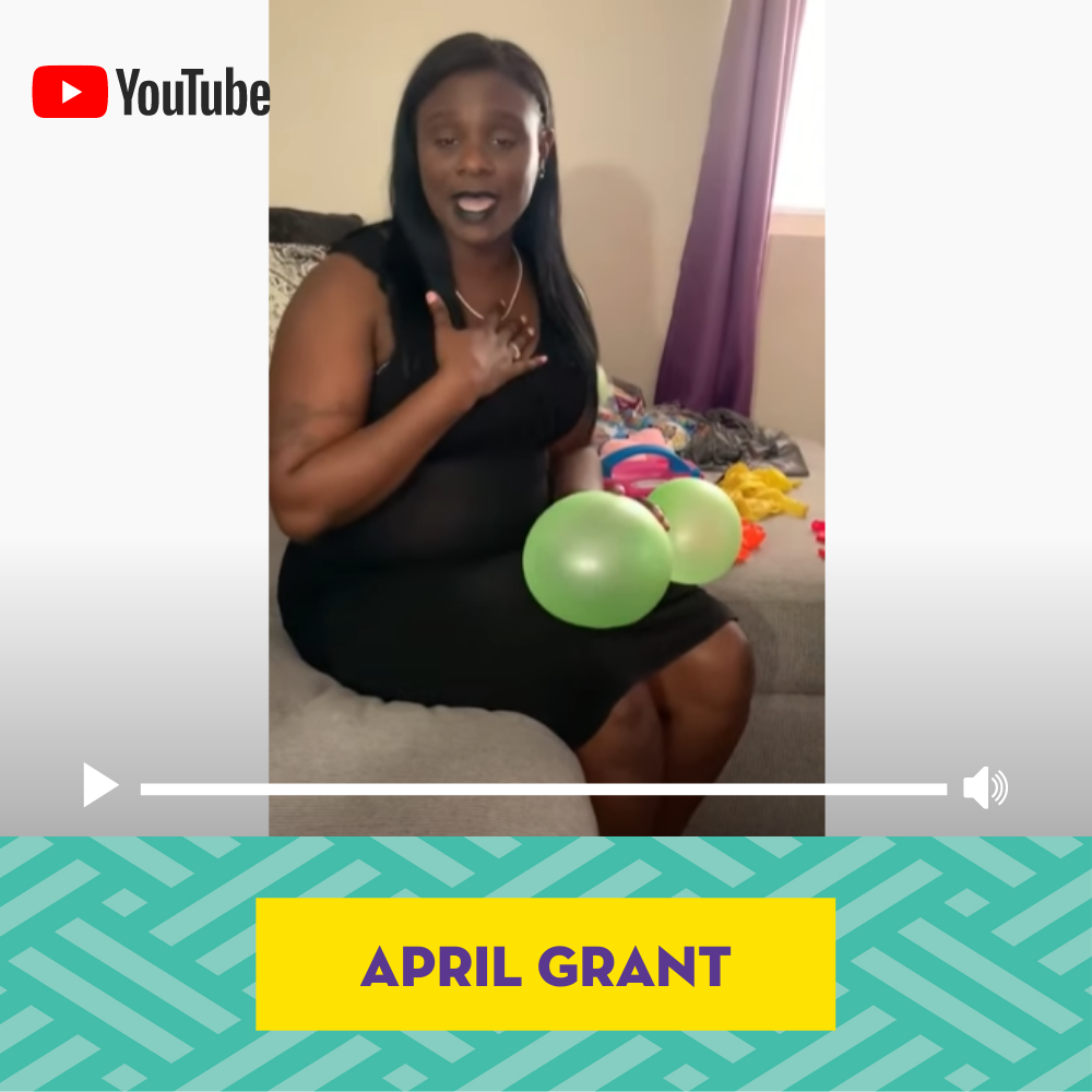 Woman sitting with two green balloons, wearing a black dress, in a room with colorful items around.