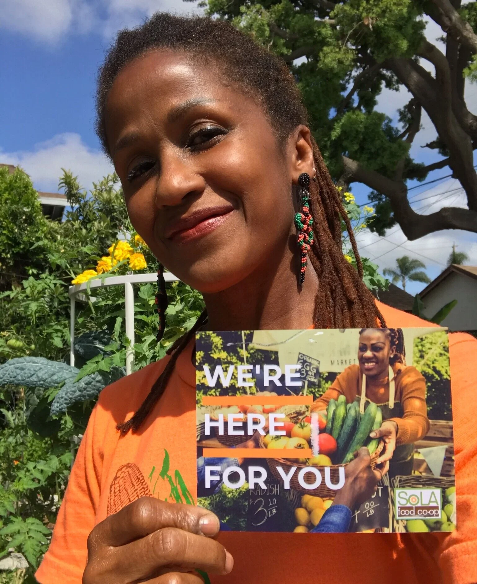 Bahni Turpin, founder of SoLA Food Co-op, holding a community invitation card outdoors in South Los Angeles.