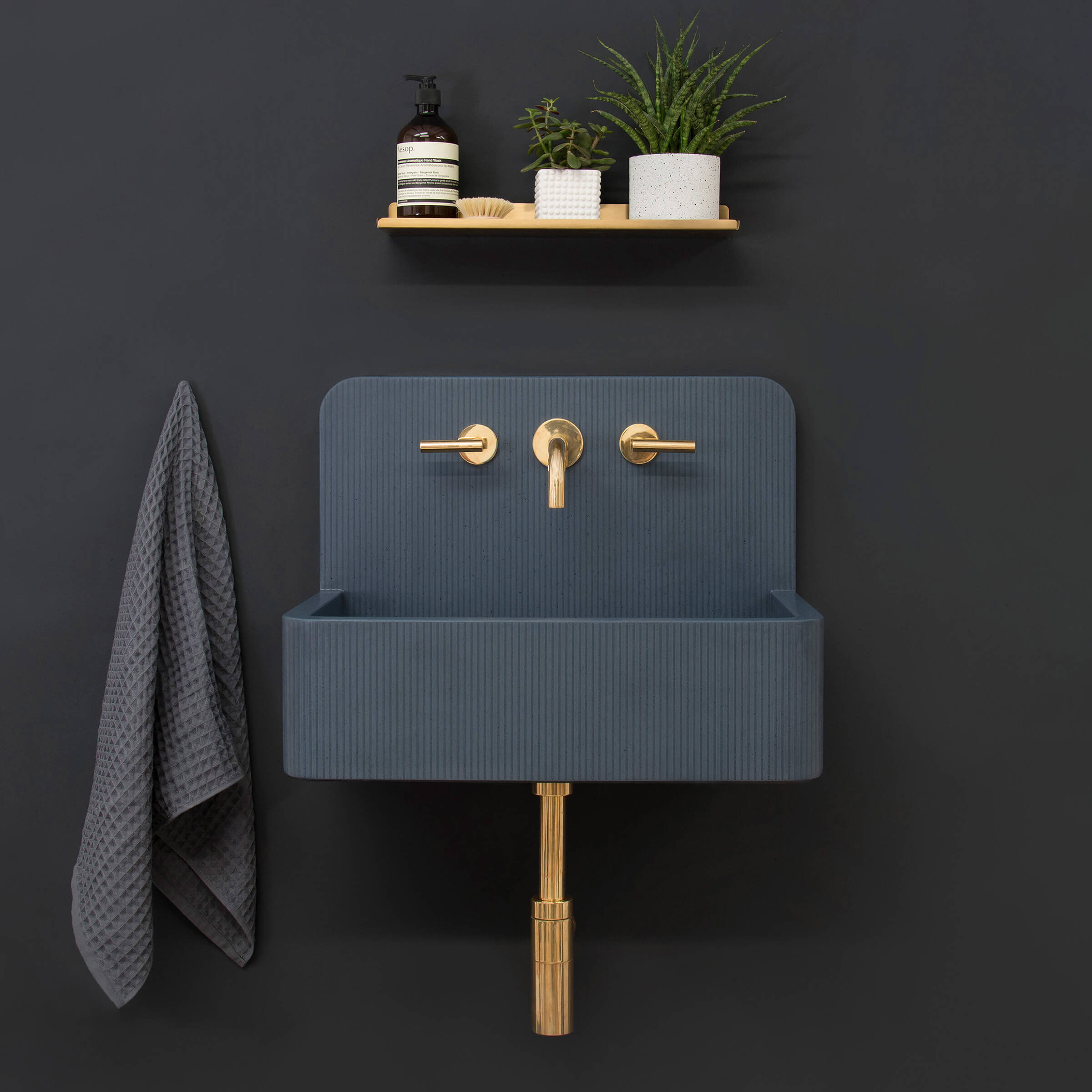 A dark navy blue wall-mounted concrete washbasin sink with integrated splashback, curved form and decorative ribbed surface pattern and brass hardware (Copy)