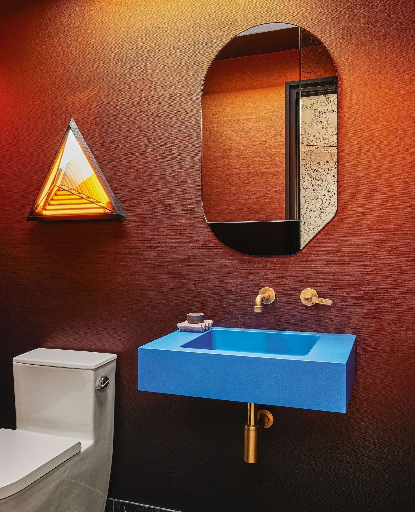 A bathroom space full of artful, fun and saturated pops. As seen in @livingetc⁠ &quot;We always try to go for maximal impact in a small space. Here, we claud the walls in the most sultry bronze wallpaper and juxtapose it with an electric-blue concret