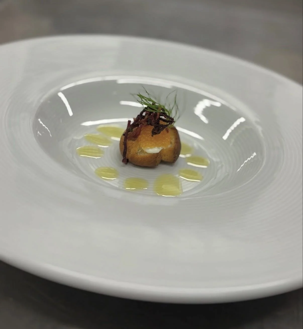 Elegant ensam dessert med en liten bakelse, toppad med växt och serverad på en vit tallrik med oljebaserad dekoration.