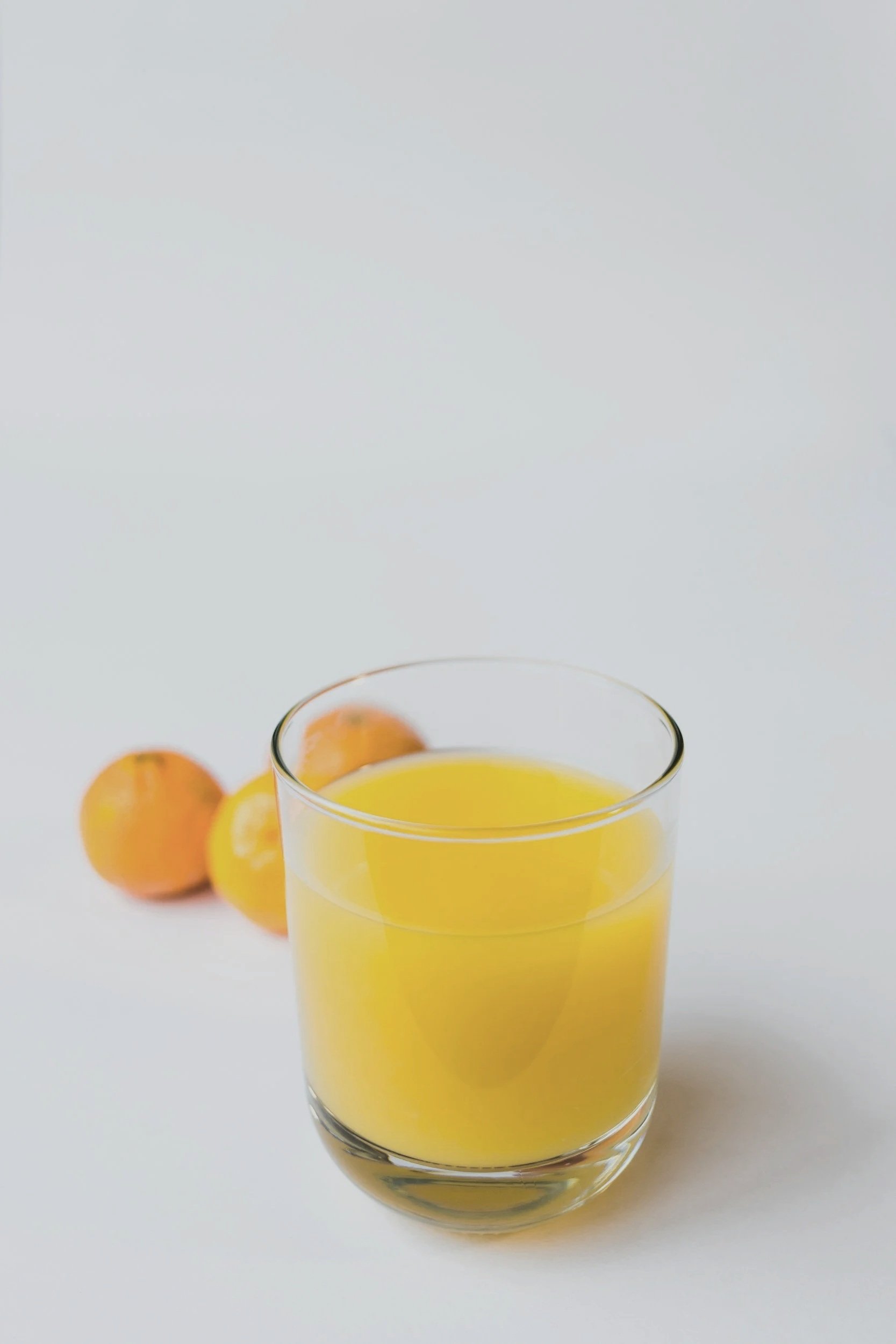 Ett glas med gul vätska, troligen juice, på ett vitt underlag med tre aprikoser i bakgrunden.