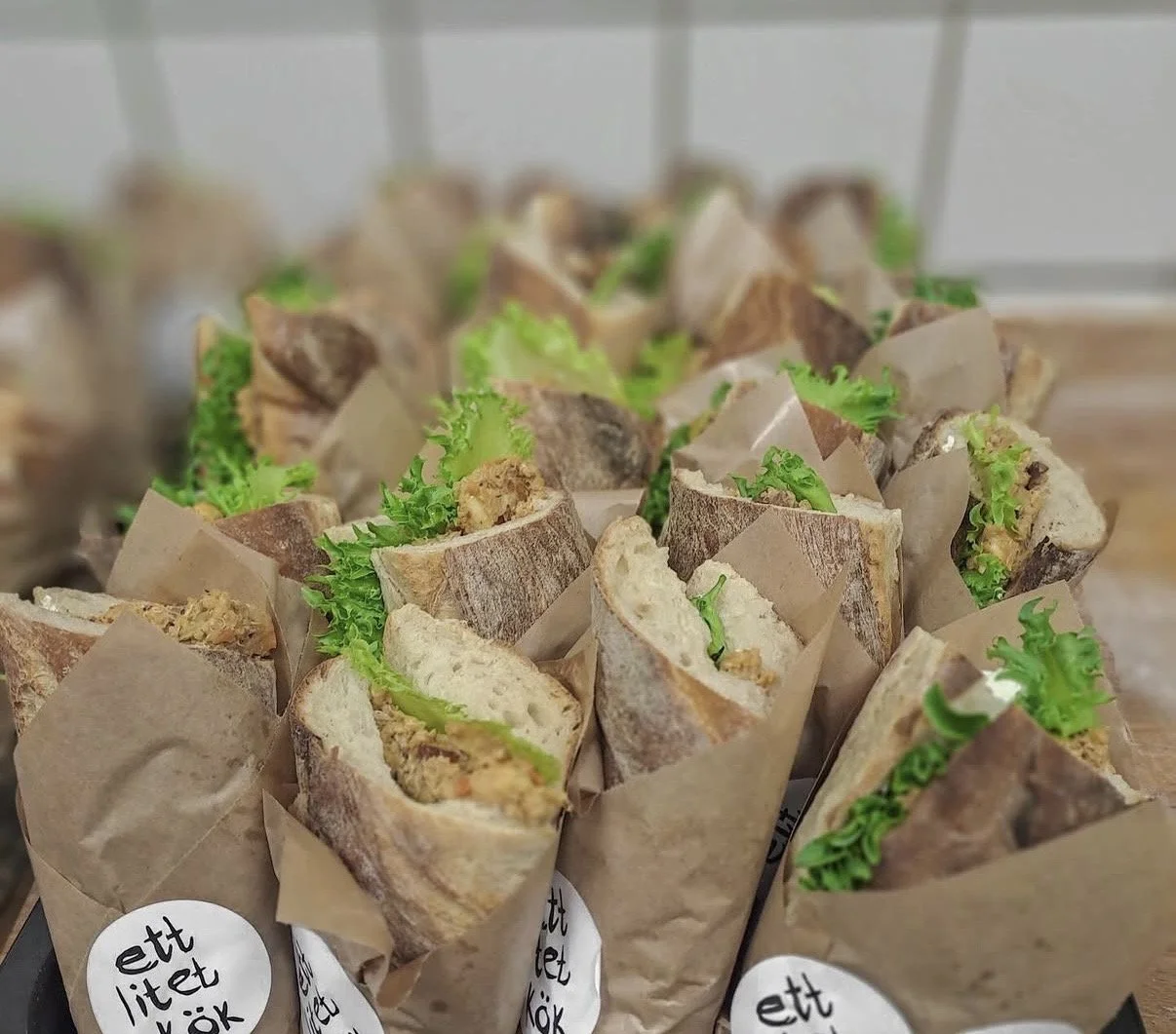 Smörgåsar med sallad i bröd, inslag av grönt, inneslutna i papper.