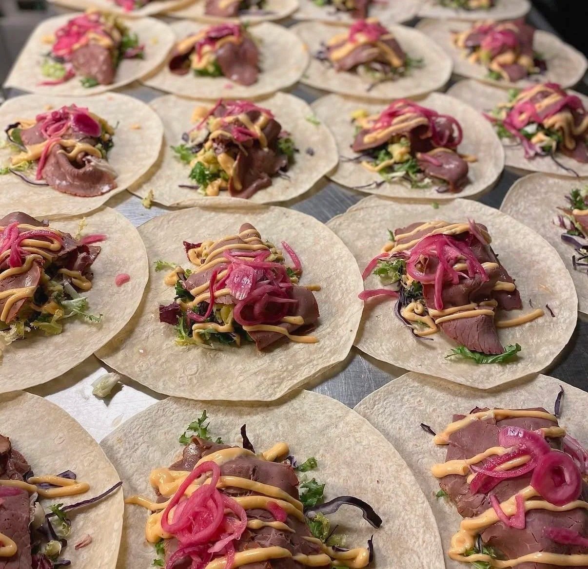 Flera tacos med fyllning av kött, sallad, inlagd rödlök och dressingsås.