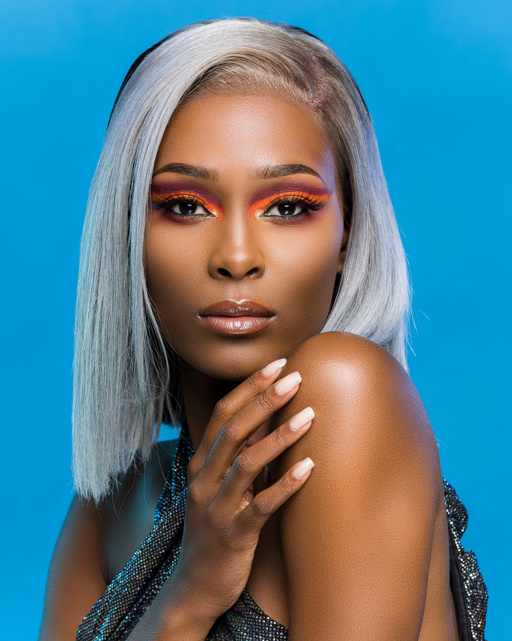 A woman with silver hair and vibrant makeup posing against a blue background.