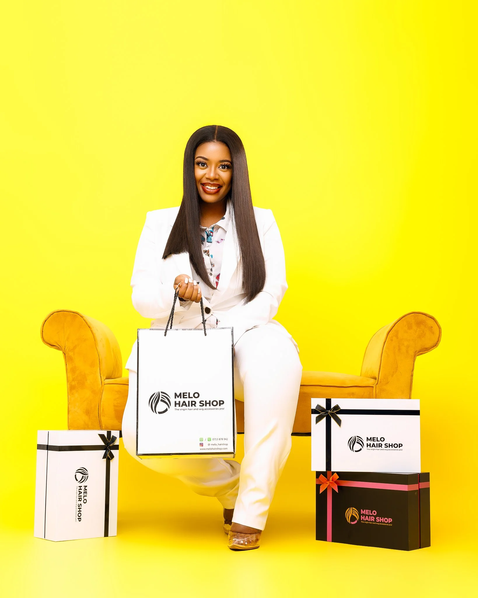 Smiling woman in white suit holding shopping bag in front of yellow background, with boxes branded 'Melo Hair Shop' beside her.