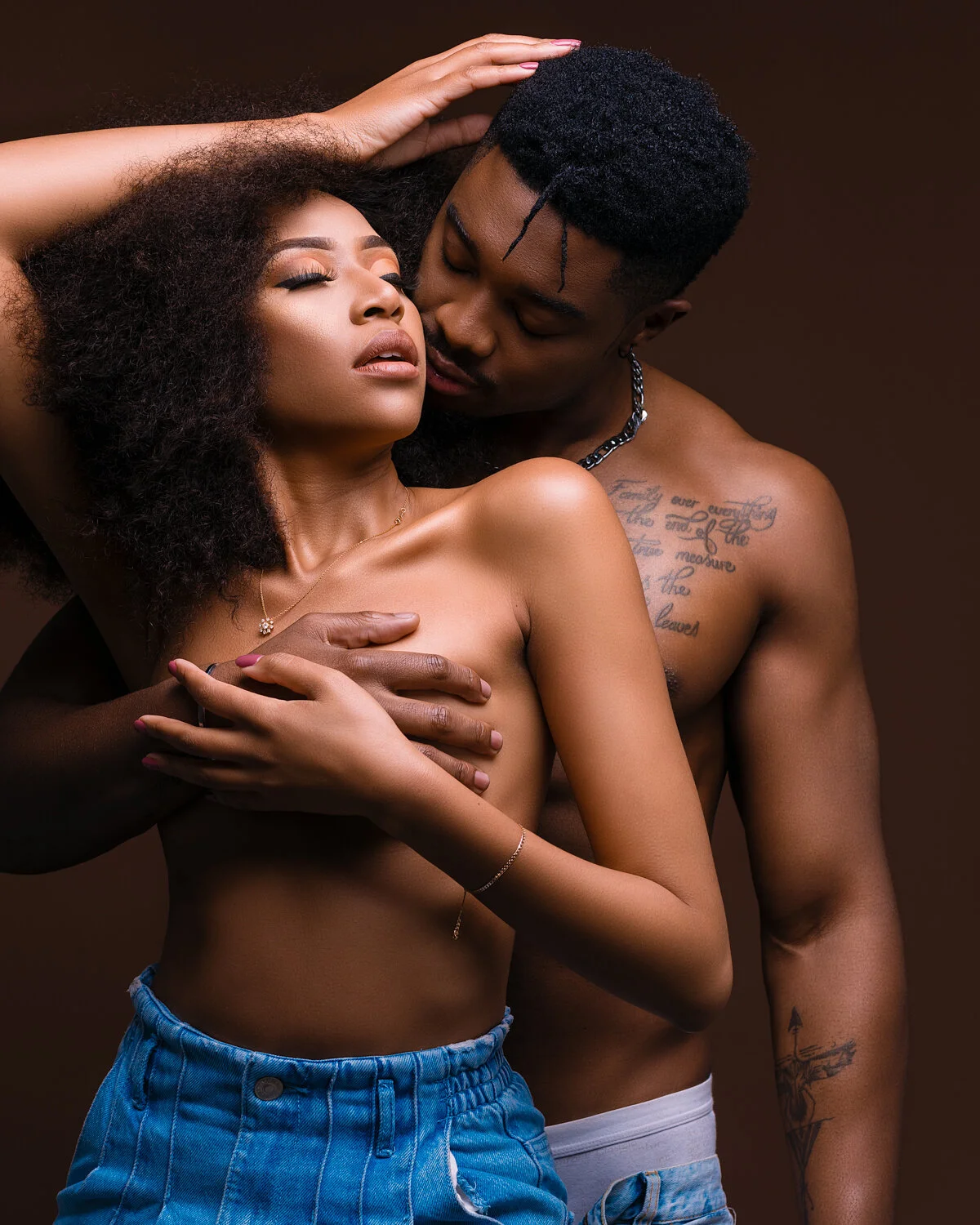 A man and a woman are close together, embracing intimate contact. The woman has her eyes closed, her head tilted back, and her hand on the man's shoulder. The man has his eyes closed and is gently pressing his face towards the woman's neck. They are 