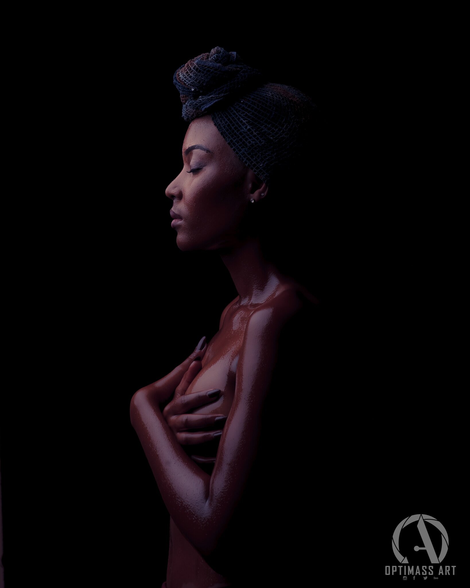 A side profile of a woman with wet skin, eyes closed, wearing a dark hair towel on her head, holding her chest with her hands, against a black background.