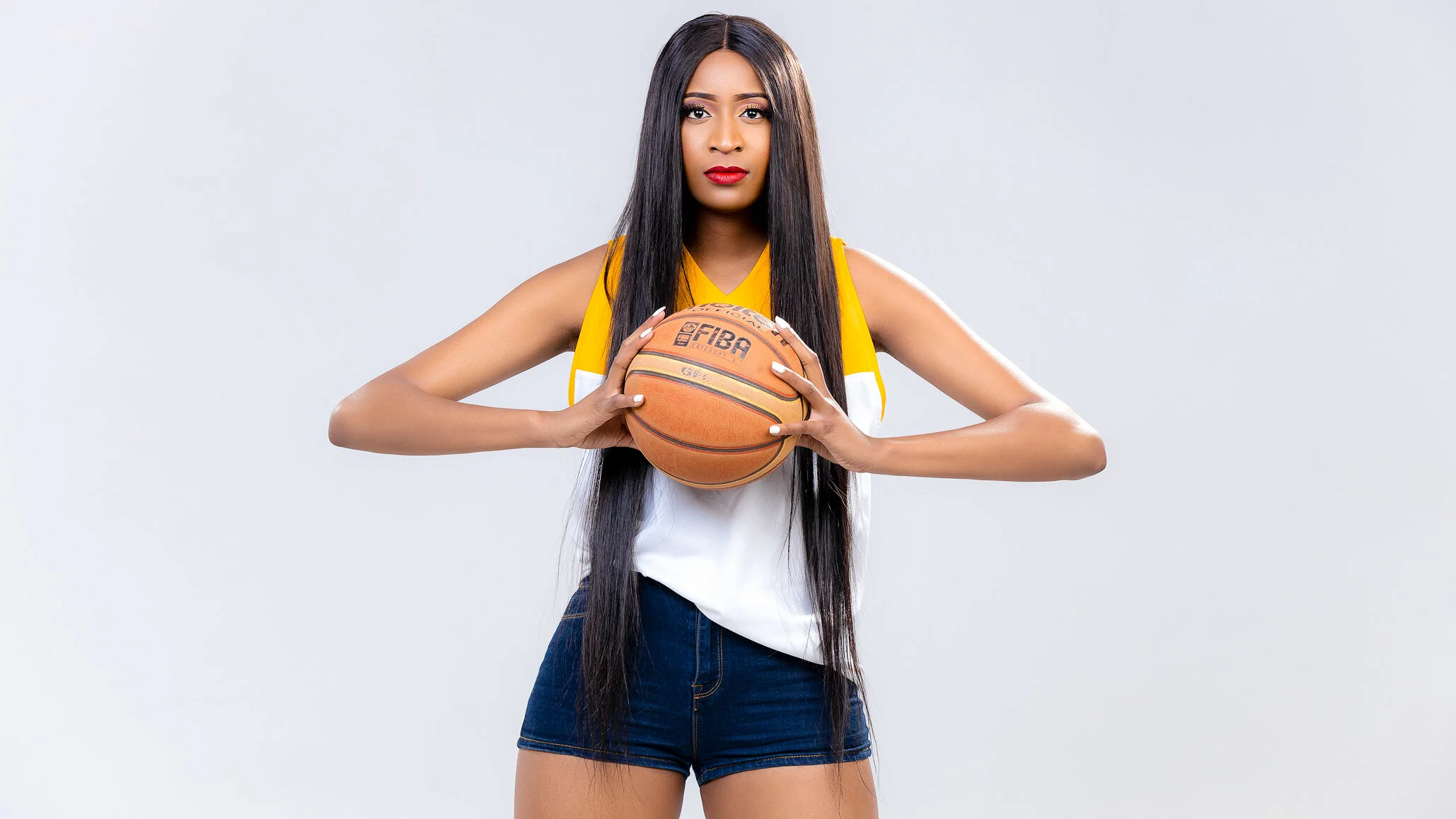 A young woman in a yellow and white sports jersey holding a basketball against a plain white background.